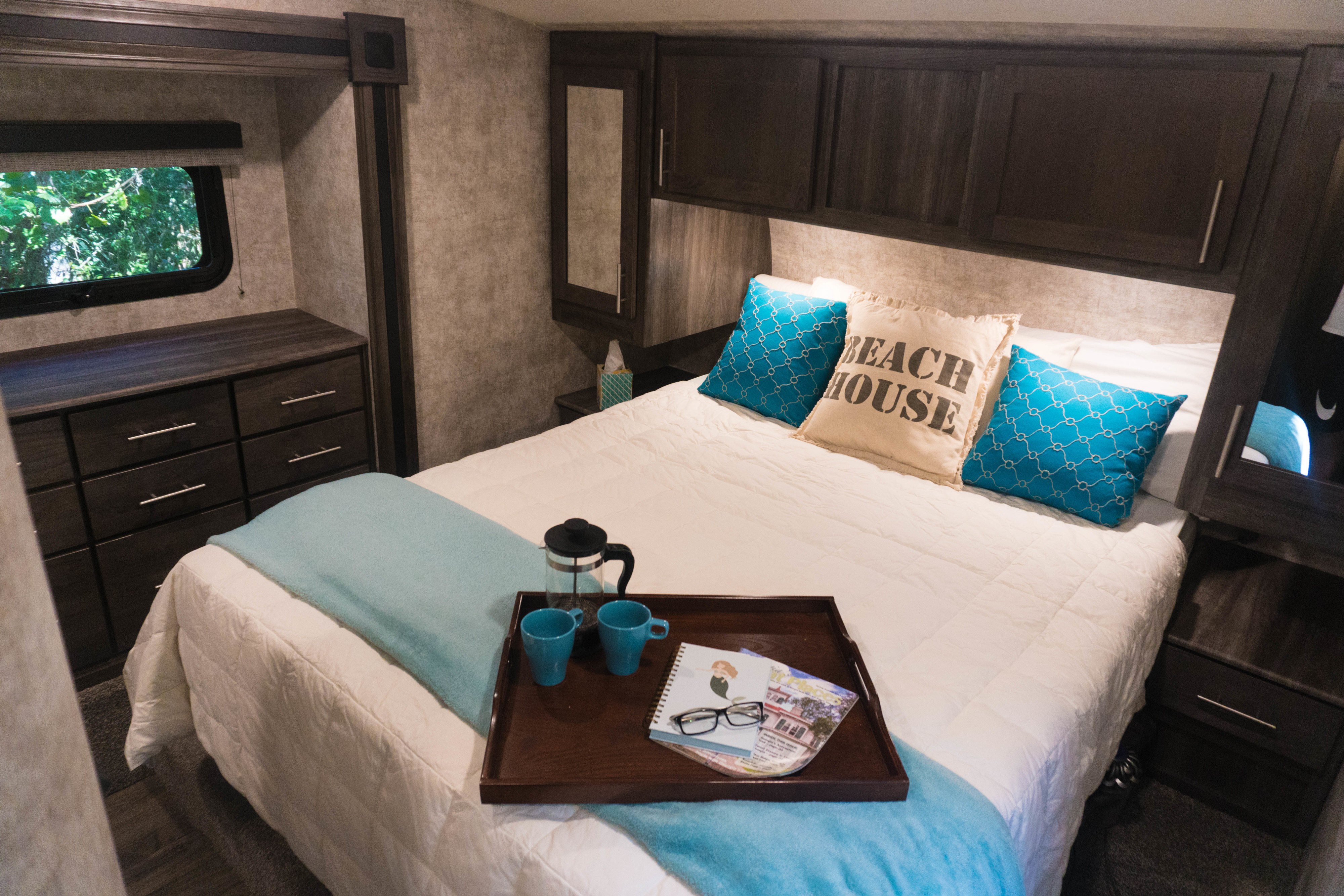 Cozy RV rental bedroom featuring a queen bed, built-in storage, and a welcoming coffee tray for comfortable travel.. Open Range Light 2018