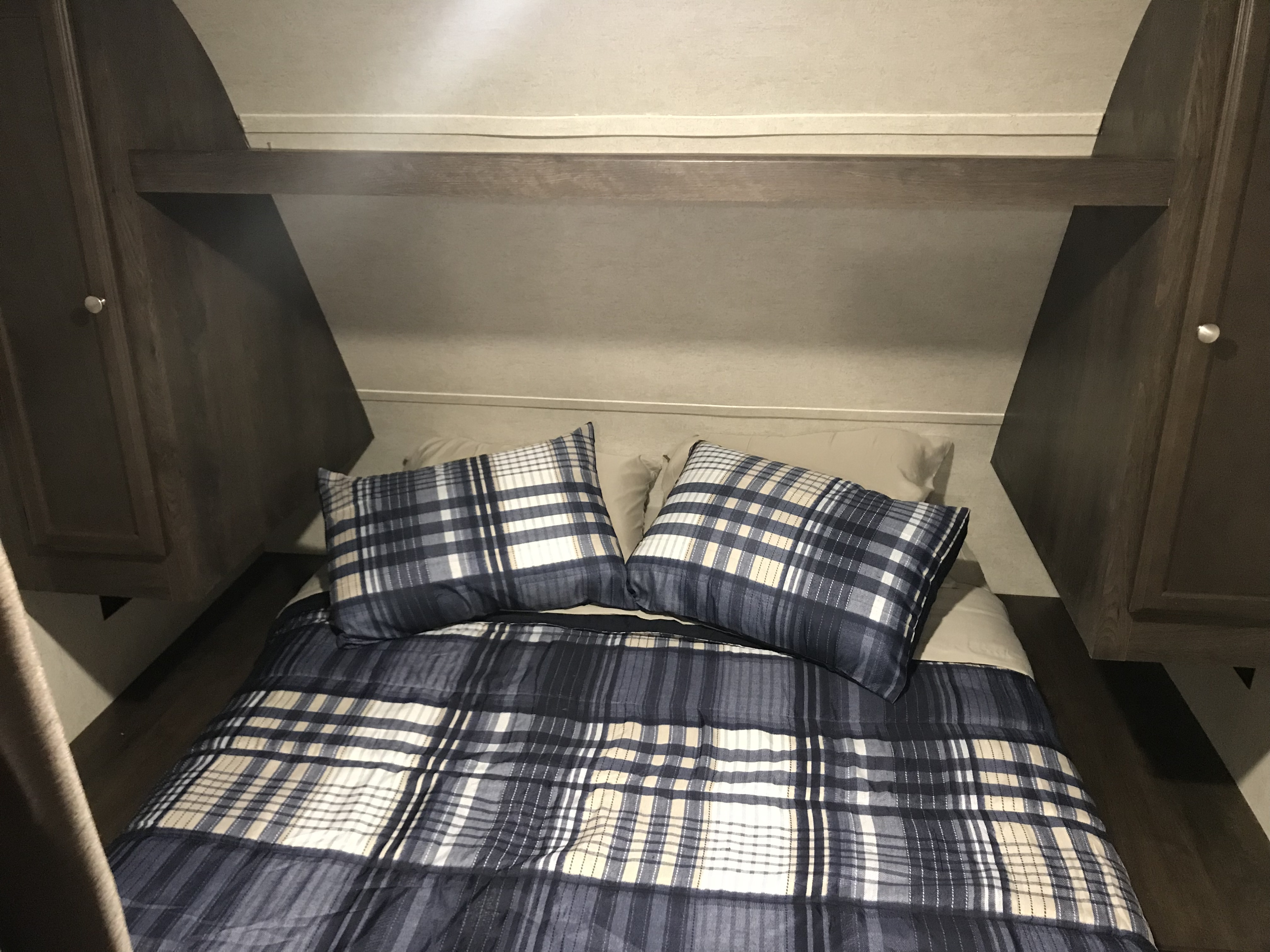Plaid bedding on a comfortable bed within an RV rental. Features compact built-in cabinets and an overhead shelf.. Starcraft Autumn Ridge 27BHS 2018