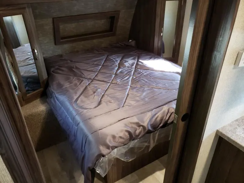 Inside an rv rental, a compact bedroom features a gray bed, built-in storage, and mirrors. Perfect for travel lodging.. Coachmen Apex 265rbss 2019