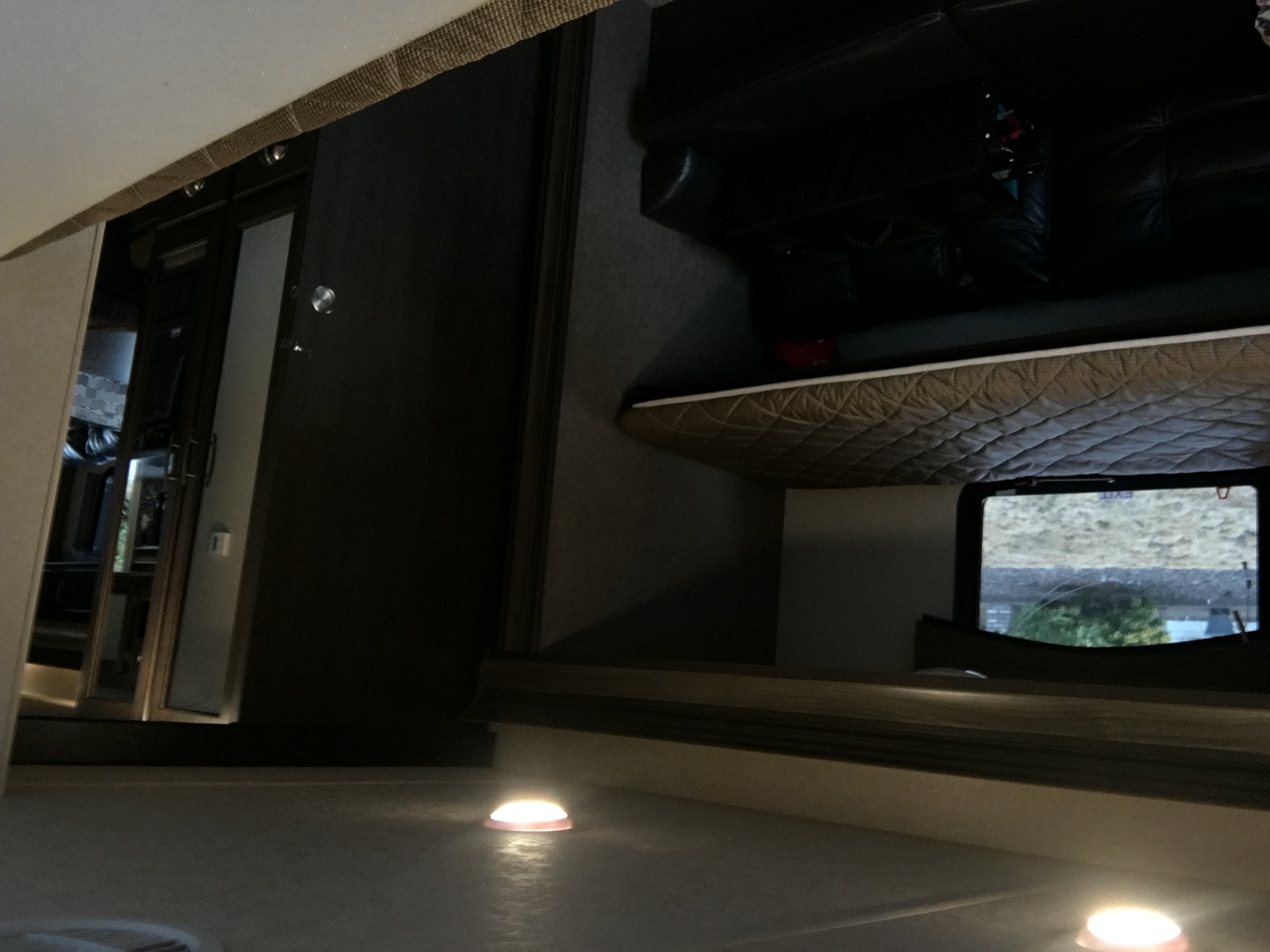 An RV rental interior: elevated sleeping area with quilted mattress, window view, and glowing floor lights. Cozy night scene.. Forest River Evo 2016