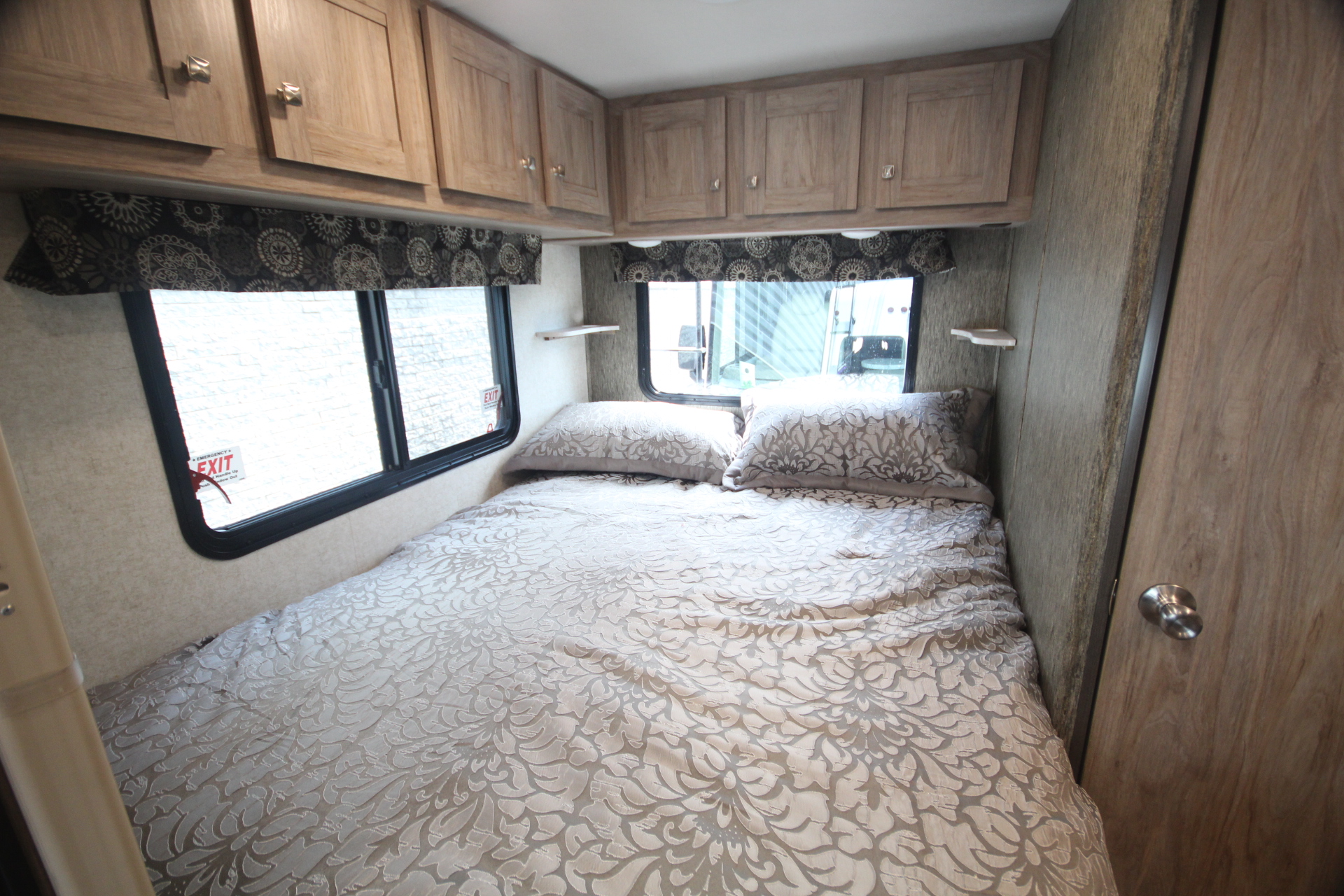 Comfortable RV rental bedroom with patterned bed, windows, and overhead cabinets, ideal for your next trip.. Other Other 2026