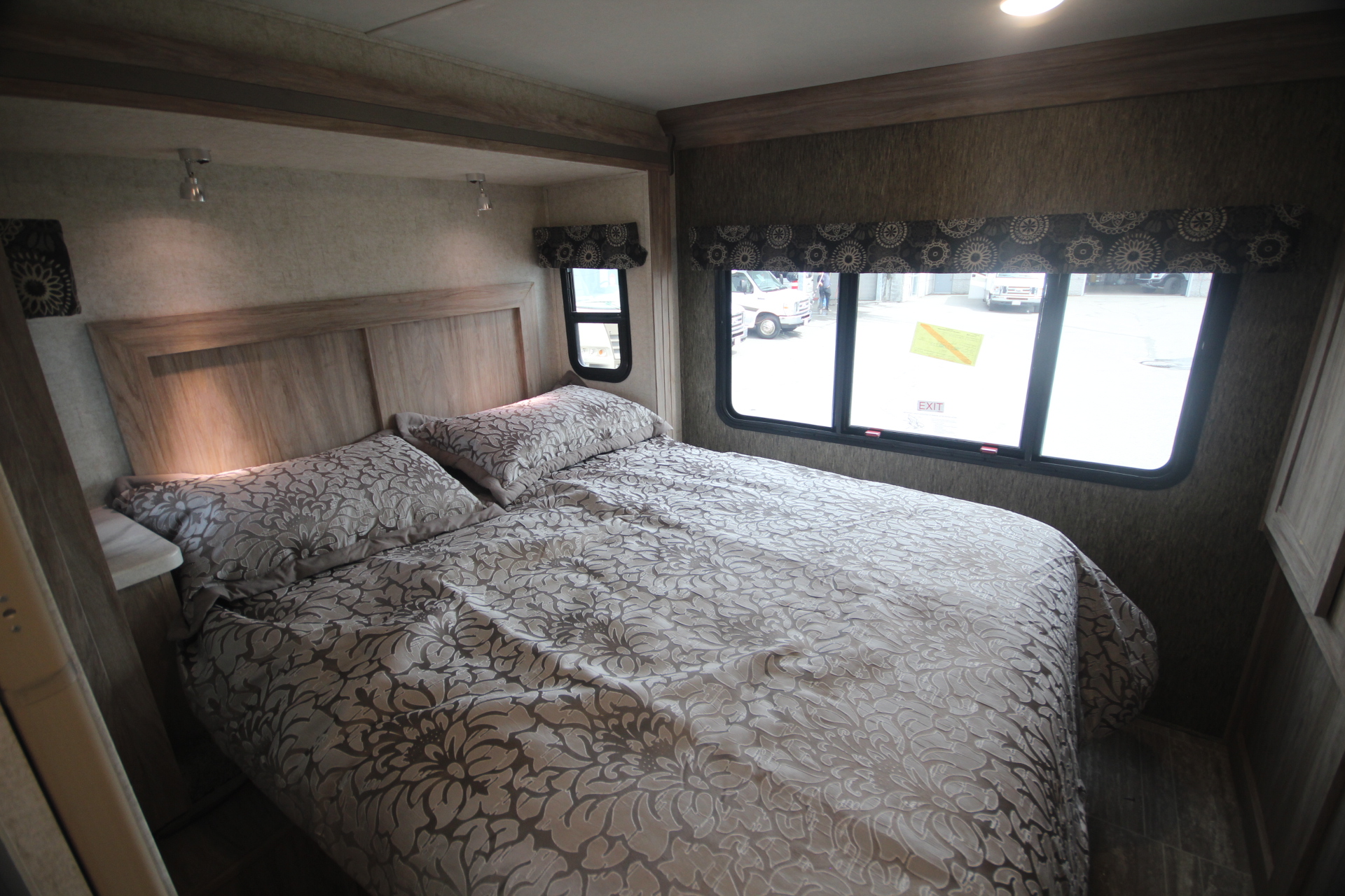 Cozy rv rental bedroom features a wooden headboard, patterned bedspread, reading lights, and windows for natural light.. Classe C C31 pieds avec extension(s) 2021