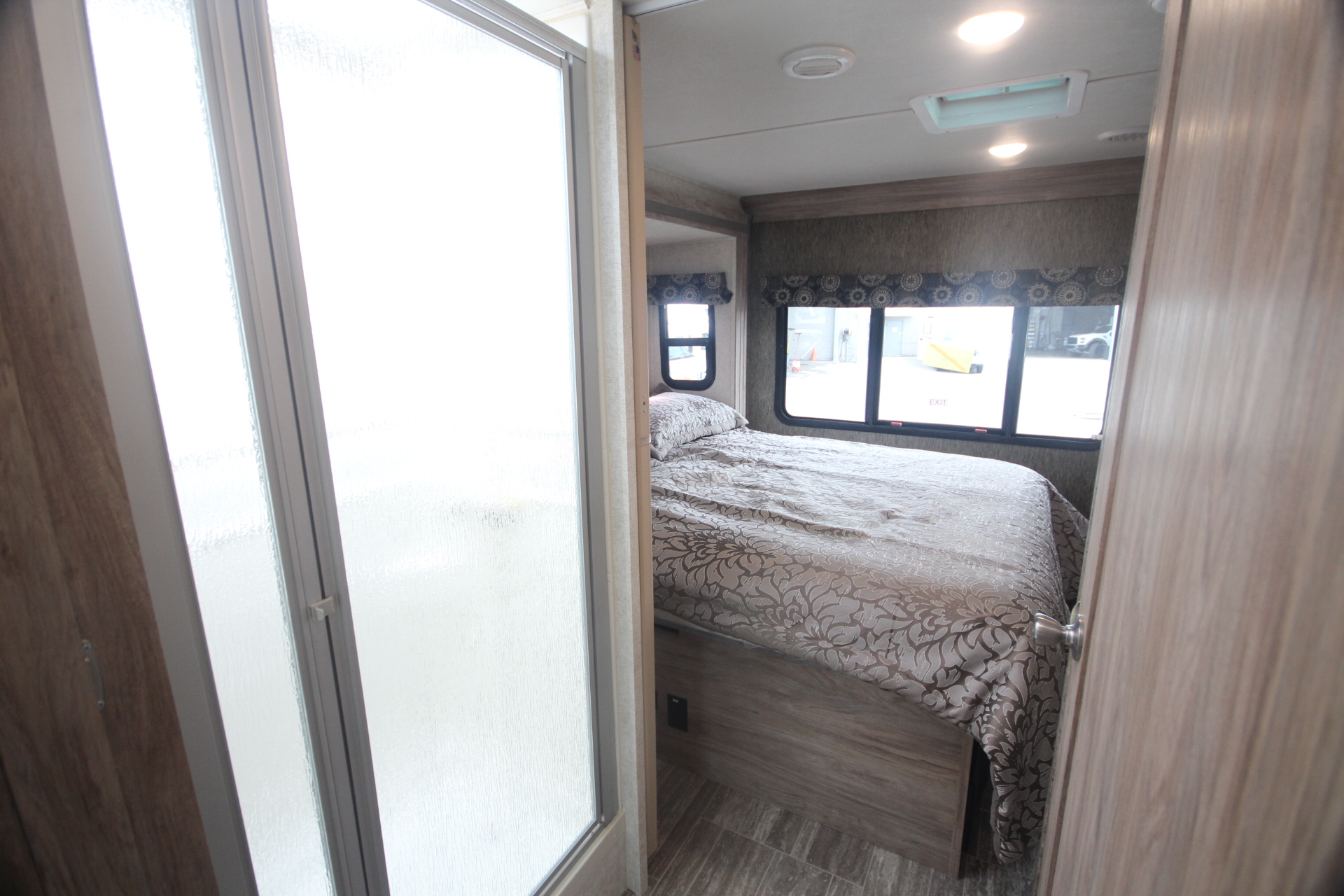 RV rental bedroom featuring a patterned bedspread and large windows, viewed from a frosted glass shower enclosure. Compact living.. Classe C C31 pieds avec extension(s) 2021