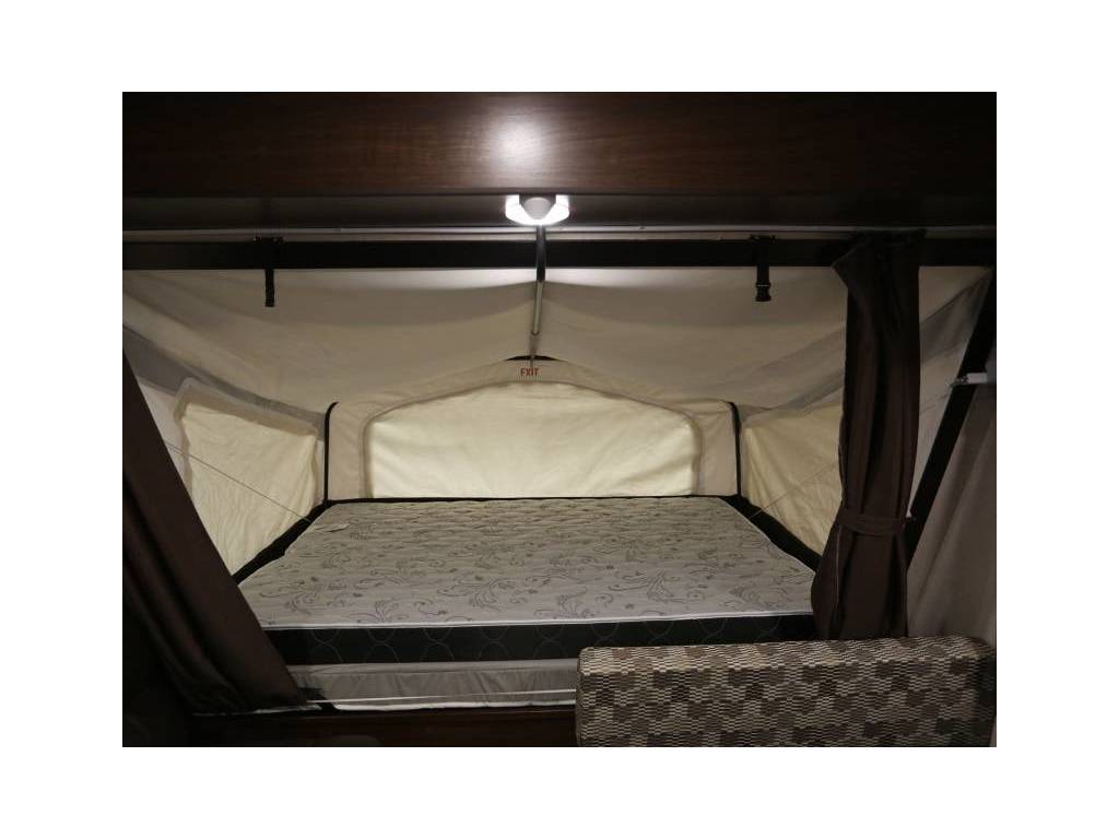 Spacious pop-up bed in an RV rental, featuring a comfortable mattress, privacy curtains, and an overhead light.. Palomino 2018 Solaire 18 foot Hybrid travel trailer sleeps 8 2018