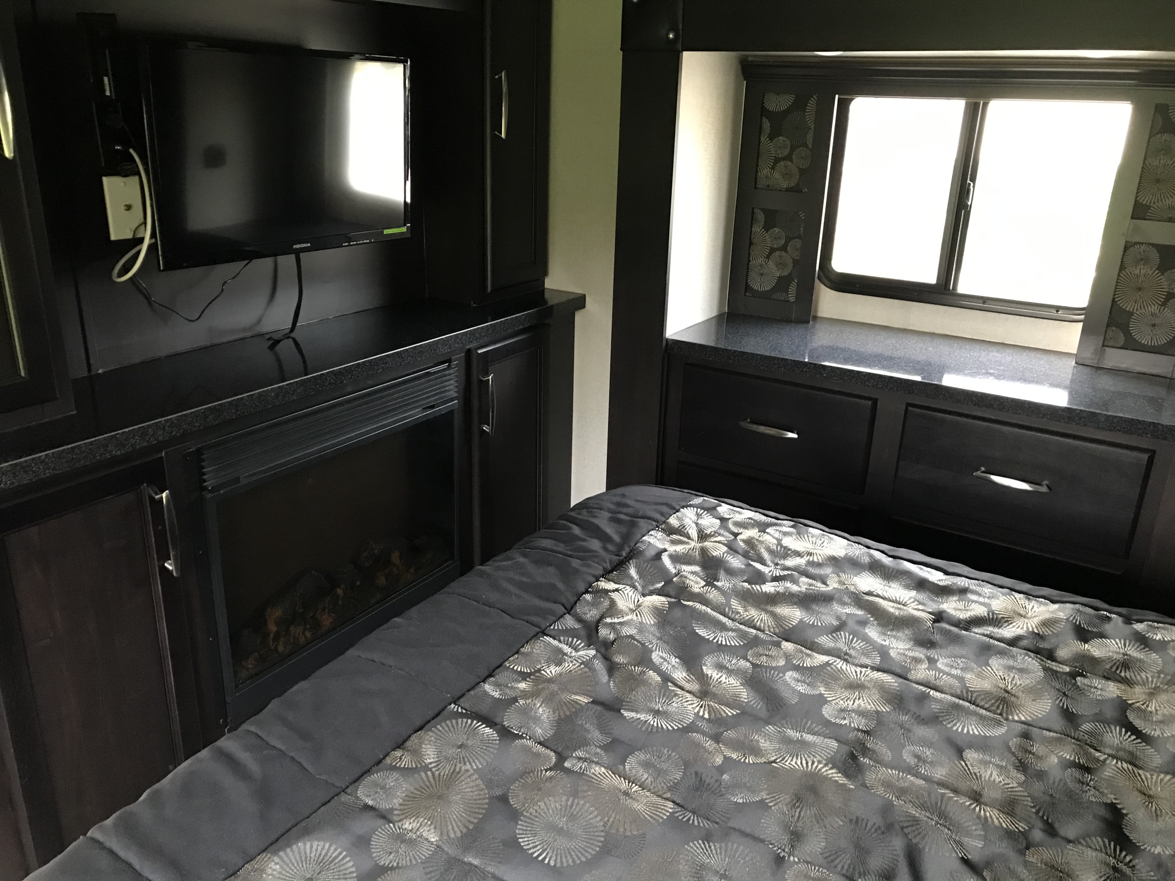 RV rental bedroom: Features dark entertainment unit with TV & fireplace, comfortable patterned bed, and bright windows.. Genesis Supreme Rv 37GS Toy Hauler 2017