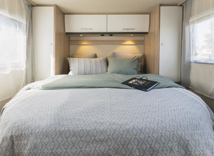 Relax in your RV rental's cozy bedroom featuring soft bedding, integrated storage, and reading lights above the bed.. Sunlight T69LC 2024