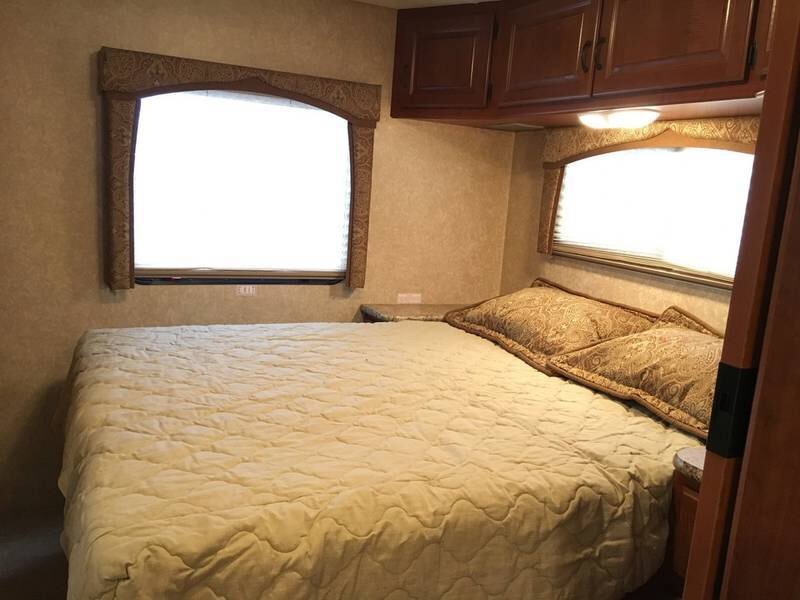 Cozy RV rental bedroom: Features a comfortable bed, two windows with shades, and overhead storage cabinets.. Ford Hurricane 2011