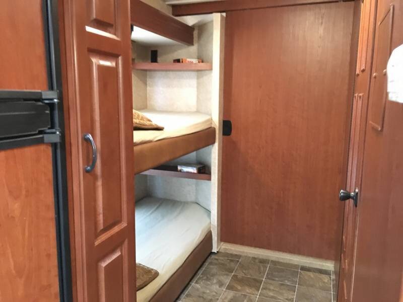 RV rental interior showing a refrigerator, two bunk beds with storage shelves, and a wooden sliding door.. Ford Hurricane 2011