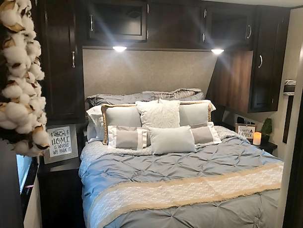 Relax in this cozy RV rental bedroom: comfy bed, soft pillows, overhead cabinets, and charming decor like the 'Home is where we park it' sign.. Jayco Flight 2018