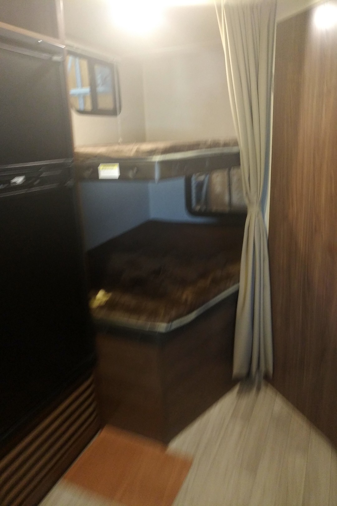 Inside an RV rental, showing bunk beds ready for guests. A fridge is on the left, and a privacy curtain on the right.. Coleman 244BH 2017