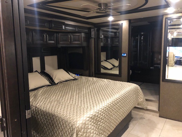 Plush RV rental bedroom showcasing a queen bed, dark wood cabinetry, a ceiling fan, and modern comforts.. American Coach American Eagle 2016