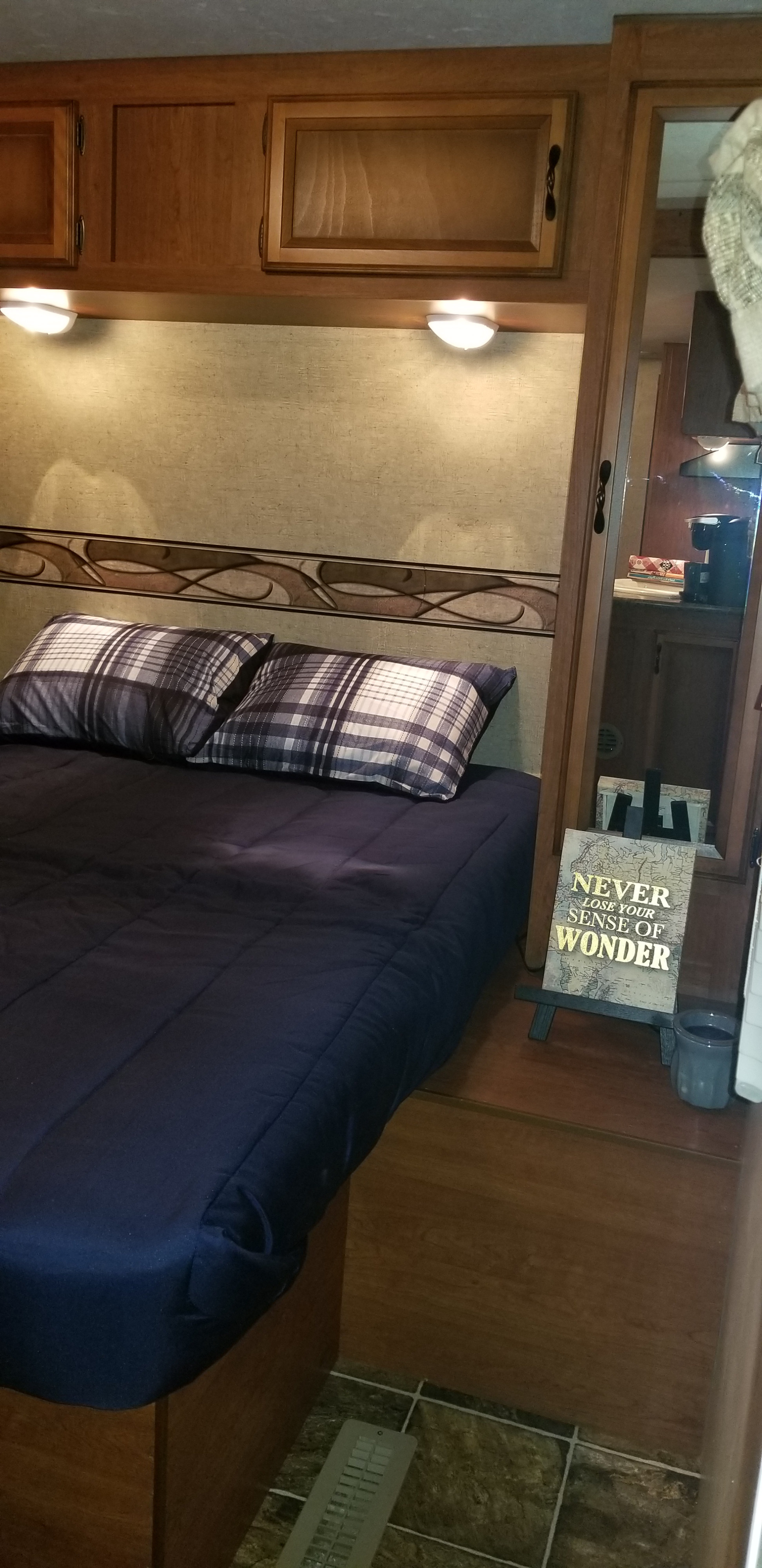 Comfortable RV rental bedroom: dark blue comforter, plaid pillows, built-in cabinets, and a 'Sense of Wonder' sign.. Other Other 2013
