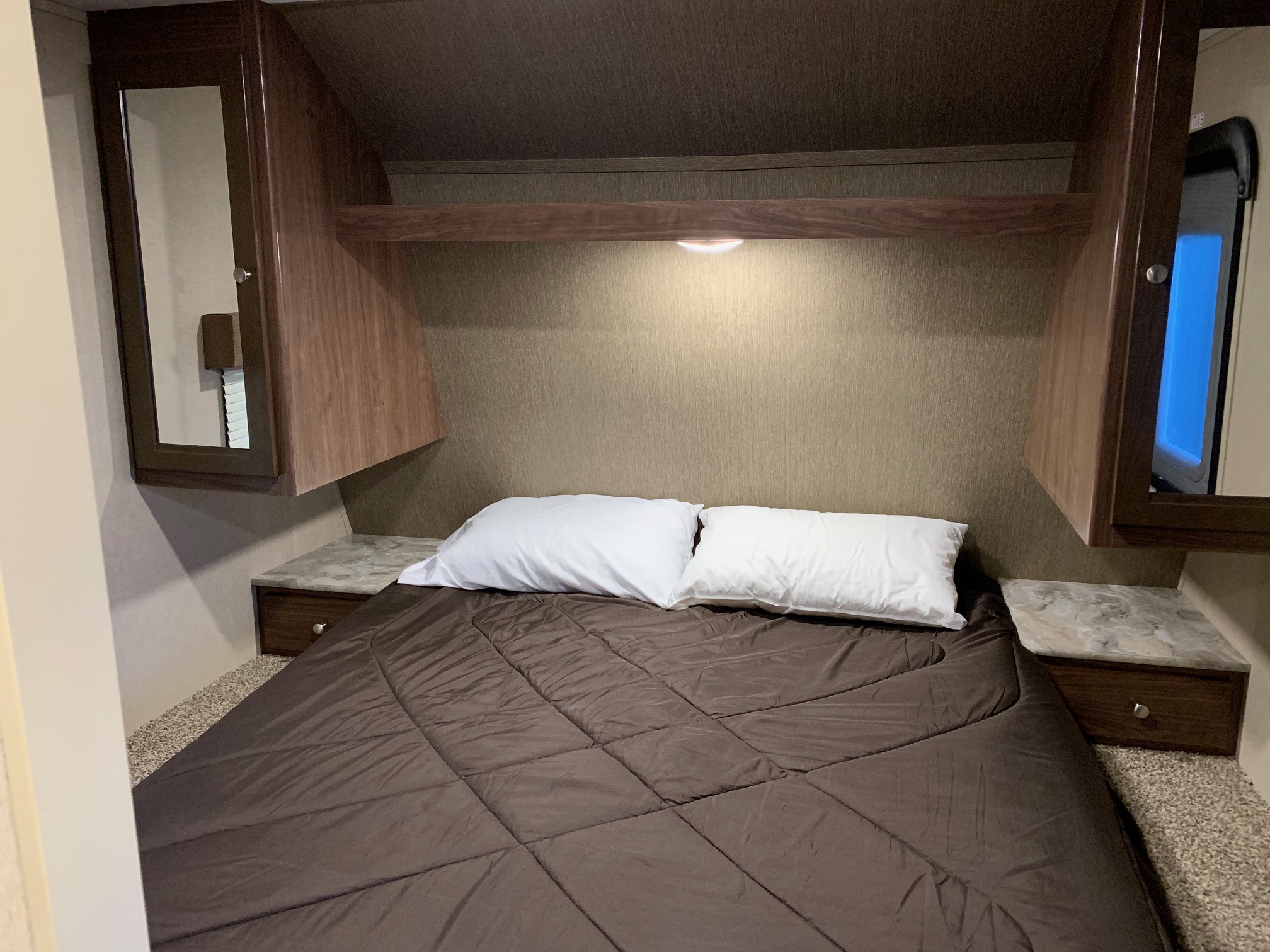 Cozy RV rental bedroom featuring a bed with white pillows, mirrored cabinets, and a window for natural light.. Coleman Lantern 2018