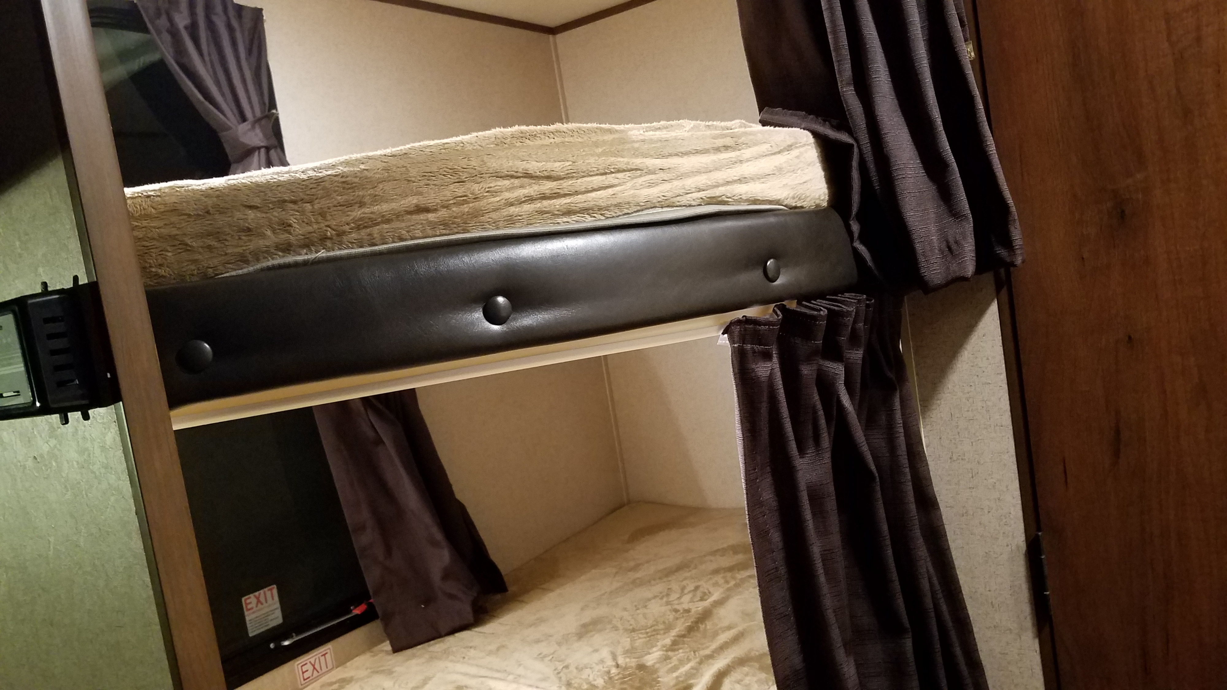 Cozy bunk beds within an RV rental, designed for compact travel. Features include dark privacy curtains and an exit sign.. Jayco Jay Flight 2016