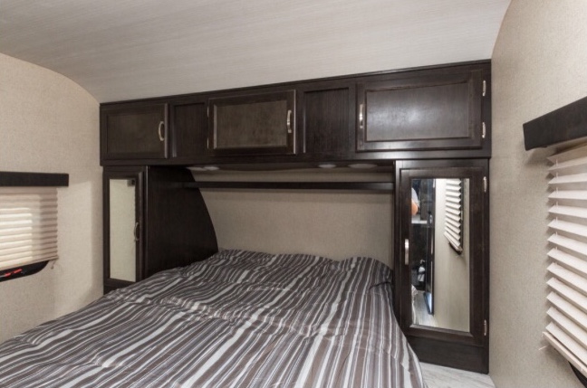 Cozy RV rental bedroom featuring a striped bed, overhead cabinets, and compact storage solutions.. Coachmen Spirit Of America 2019