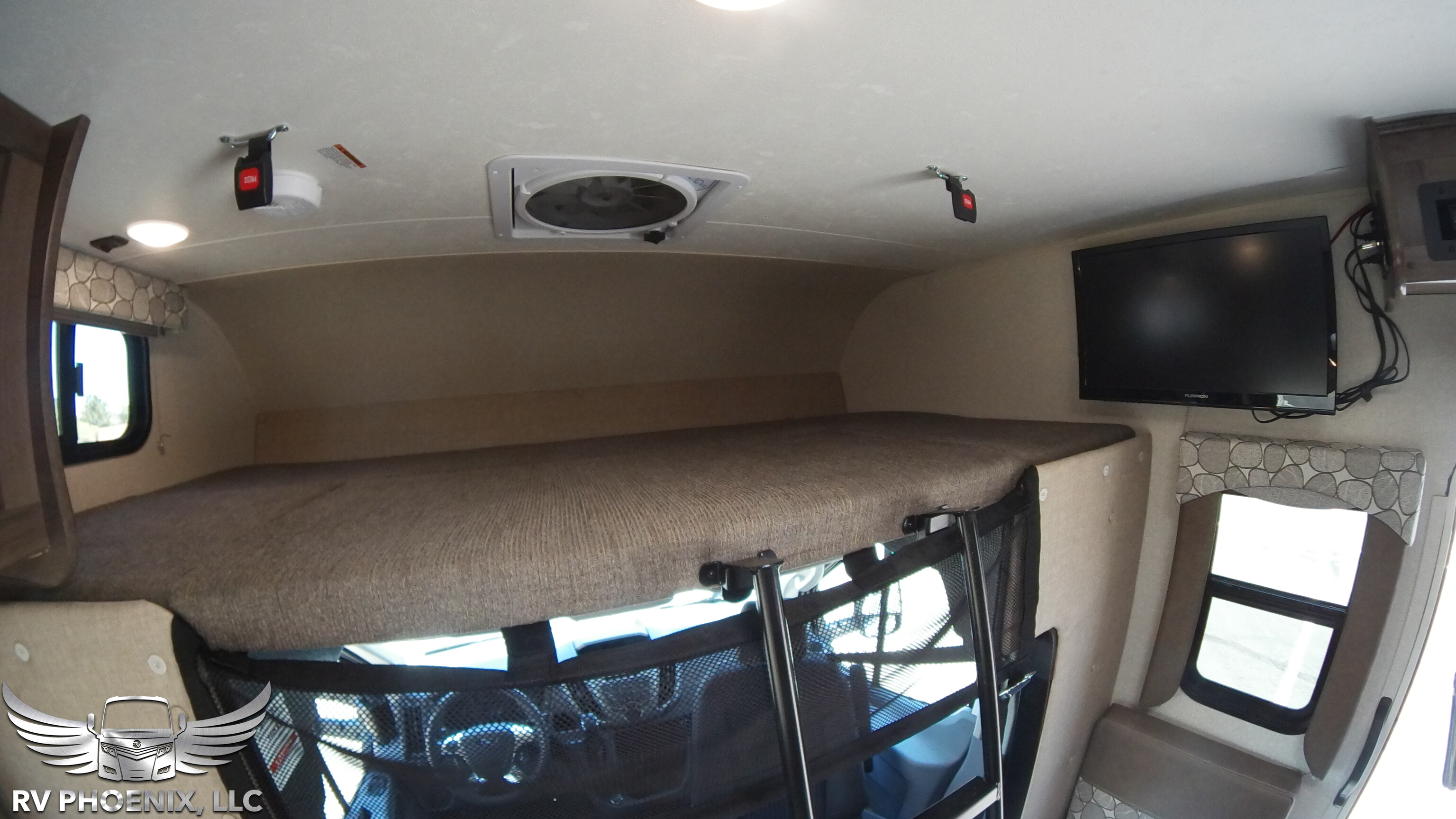 A spacious overhead bunk with safety netting, wall-mounted TV, ceiling fan, and windows inside this RV rental.. Coachmen Freelander 2019