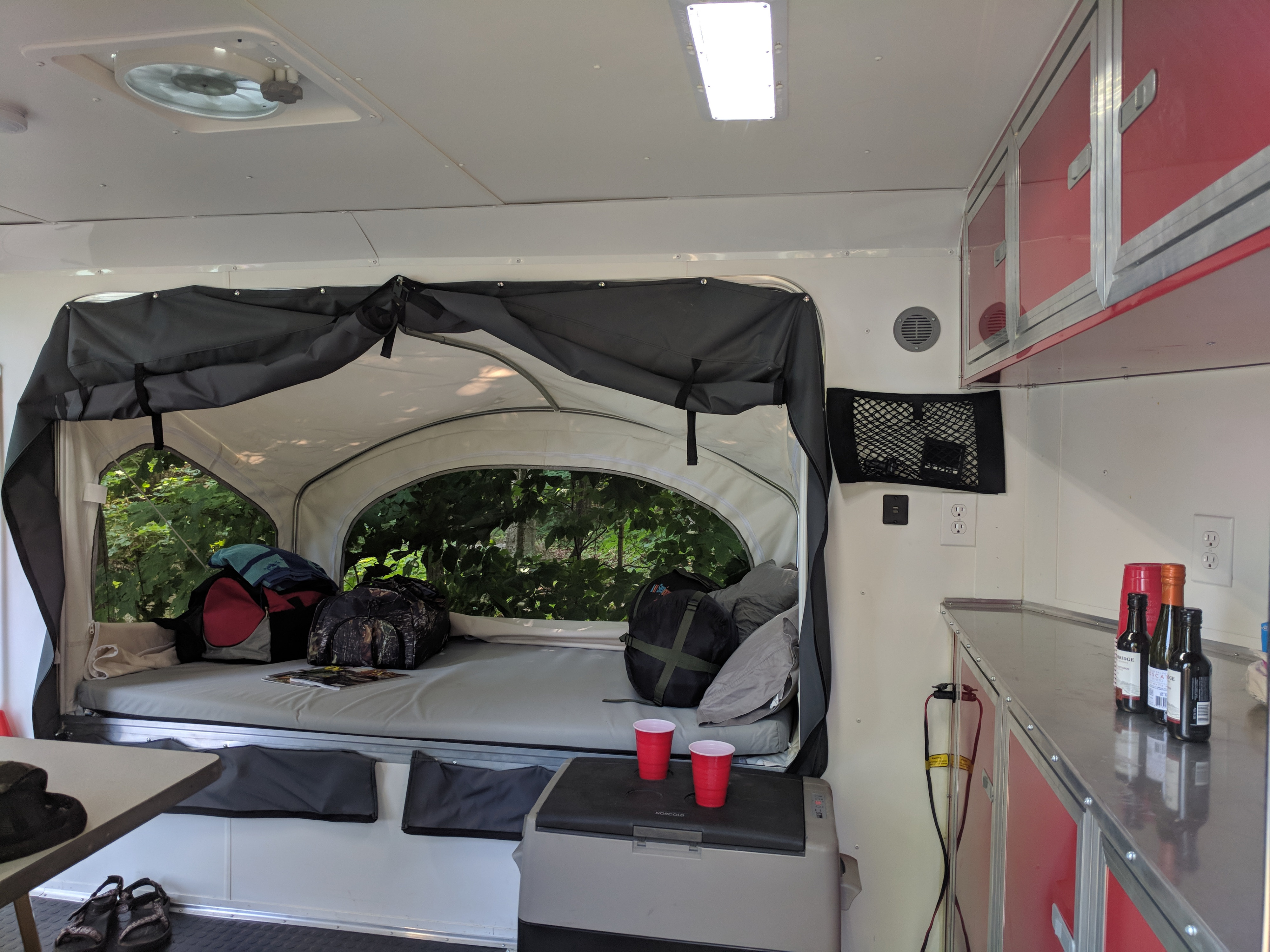 This RV rental's interior features a cozy pop-up bed with forest views, red cabinets, and a portable fridge for travel.. United XLMTV-610 2018
