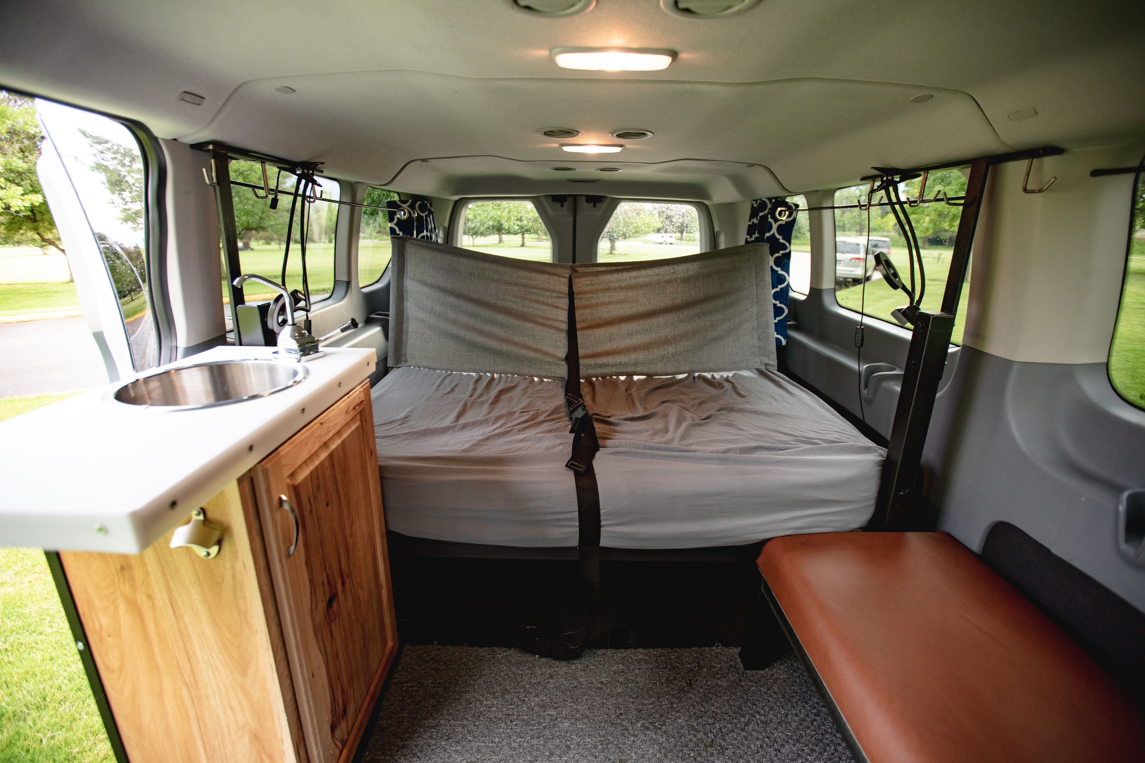 Cozy camper van interior, perfect for an rv rental adventure: bed, kitchenette with sink, and side bench.. Ford Transit 2017