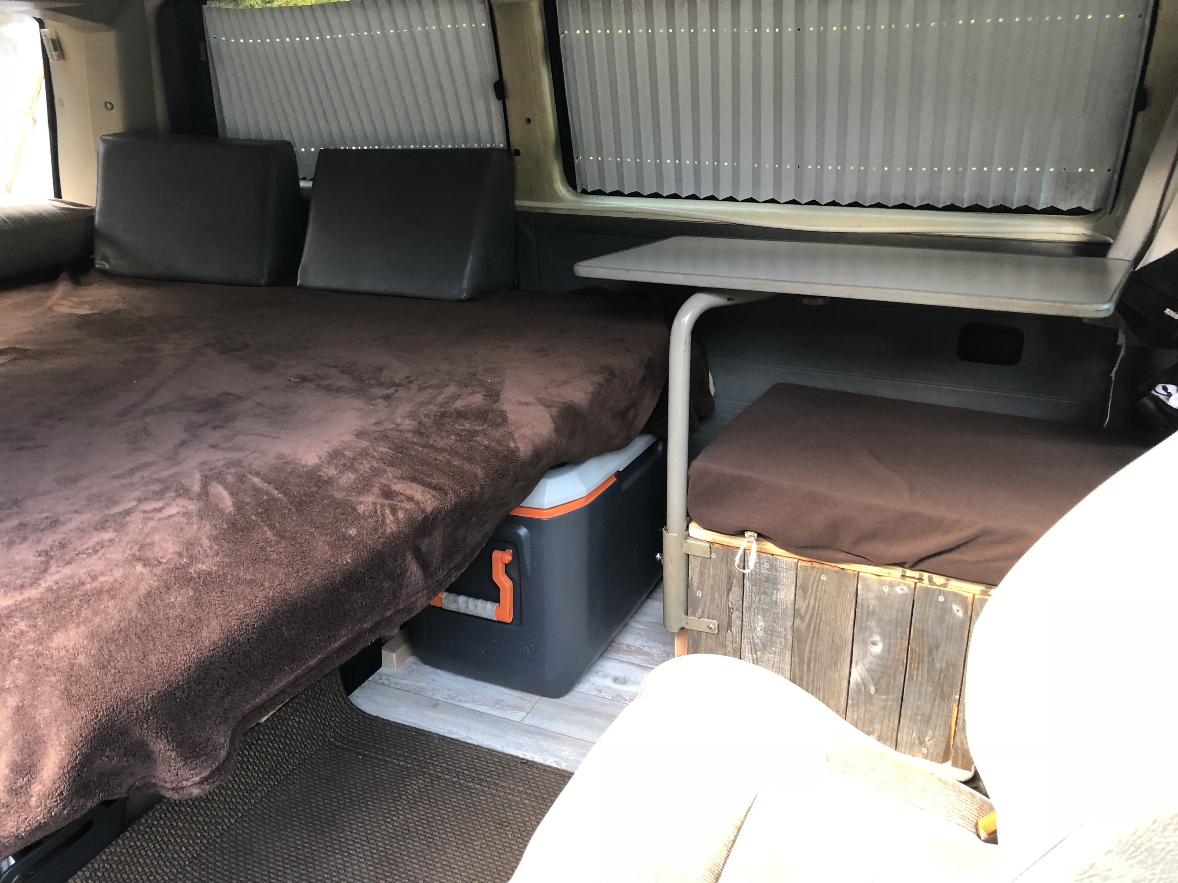 Inside this RV rental: a brown bed, cooler, and table for cozy, efficient mobile living.. VW Vanagon 1990
