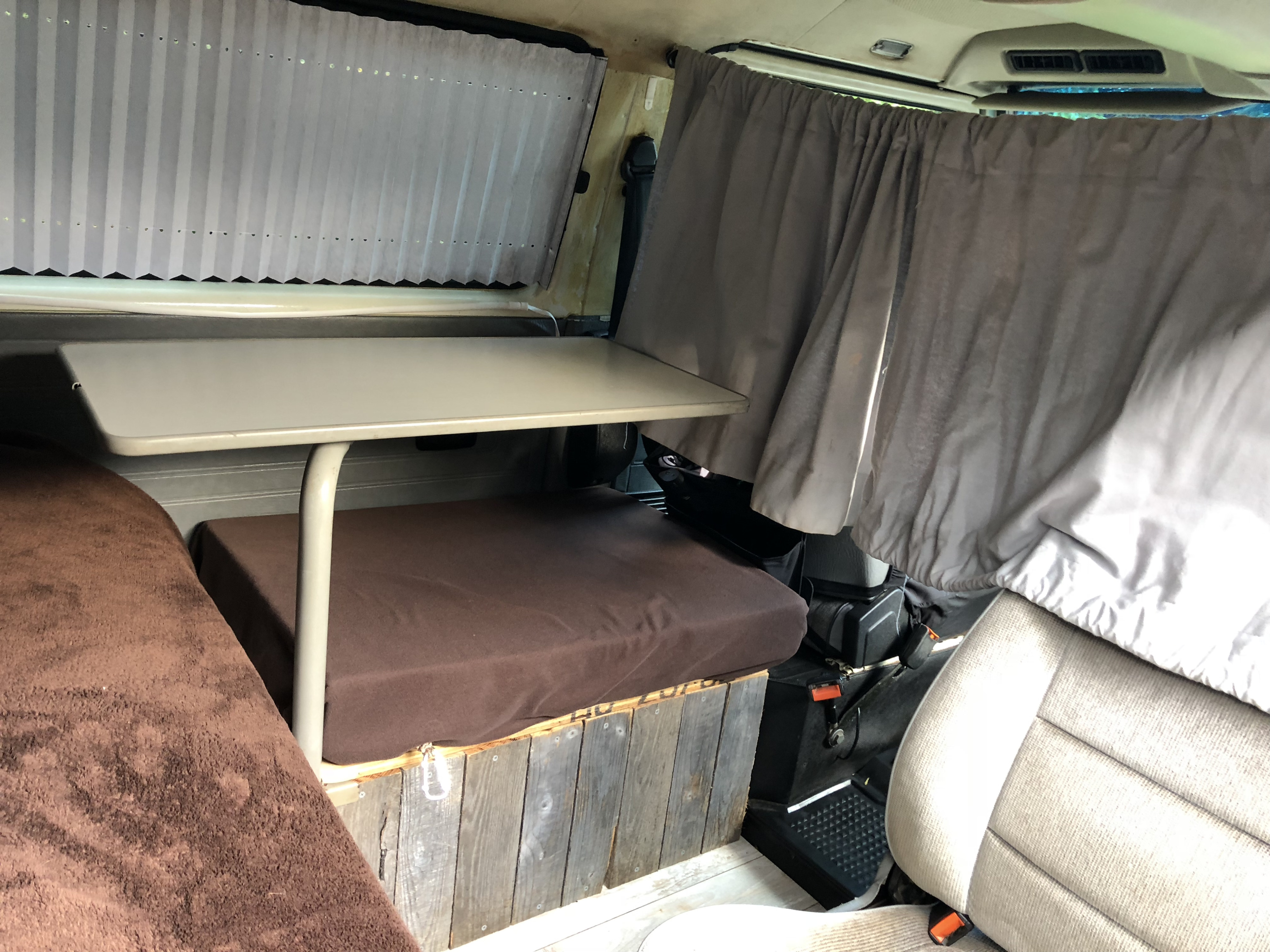 Cozy RV rental interior with convertible dinette/bed, window shades, and privacy curtains.. VW Vanagon 1990
