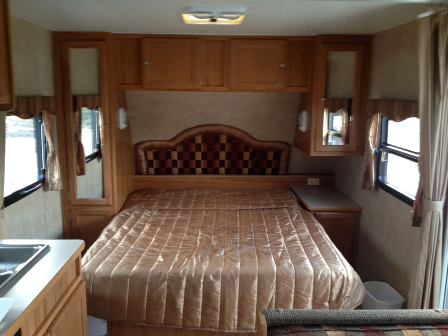 Cozy RV rental bedroom featuring a checkered headboard, comfortable bed, overhead cabinets, and bright windows.. R-Vision TS 24BH 2011