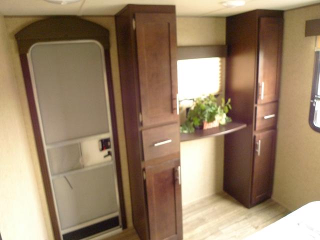 Compact RV rental interior: view of the screen door, dark wood cabinets, and a small desk with a green plant.. Forest River Grey Wolf 2018