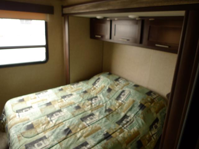 RV rental interior: A bright bedroom features a patterned bed, dark wood cabinets, and a window.. Forest River Grey Wolf 2018