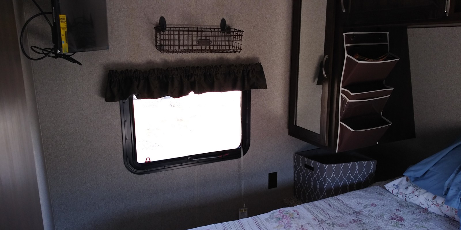 Cozy RV rental bedroom featuring a window, TV, storage basket, and hanging organizer, ready for your trip.. Keystone RV Springdale 2018