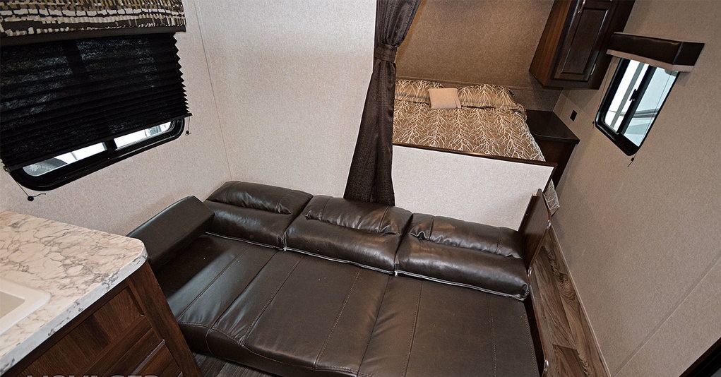 View of an RV rental's versatile interior: brown leather sofa, compact bedroom, and partial kitchen counter.. Jayco Jay Flight 2019