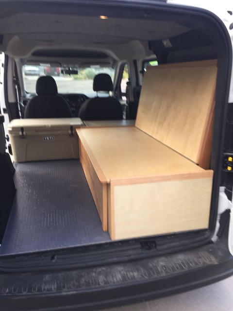 Inside an RV rental van: custom wooden bed, cooler, and front seats visible, ready for adventure.. ram promaster city 2018