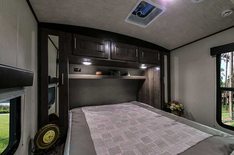 Cozy RV rental bedroom with a comfortable bed, overhead cabinets, and windows offering scenic views of nature.. Heartland Torque t322 2019
