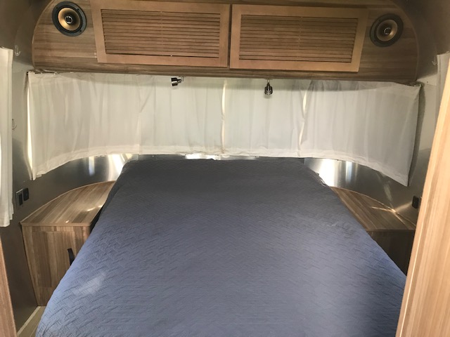 Experience comfort in this RV rental bedroom. Features a bed, wood storage, speakers, and privacy curtains.. Airstream TommyBahama 2018