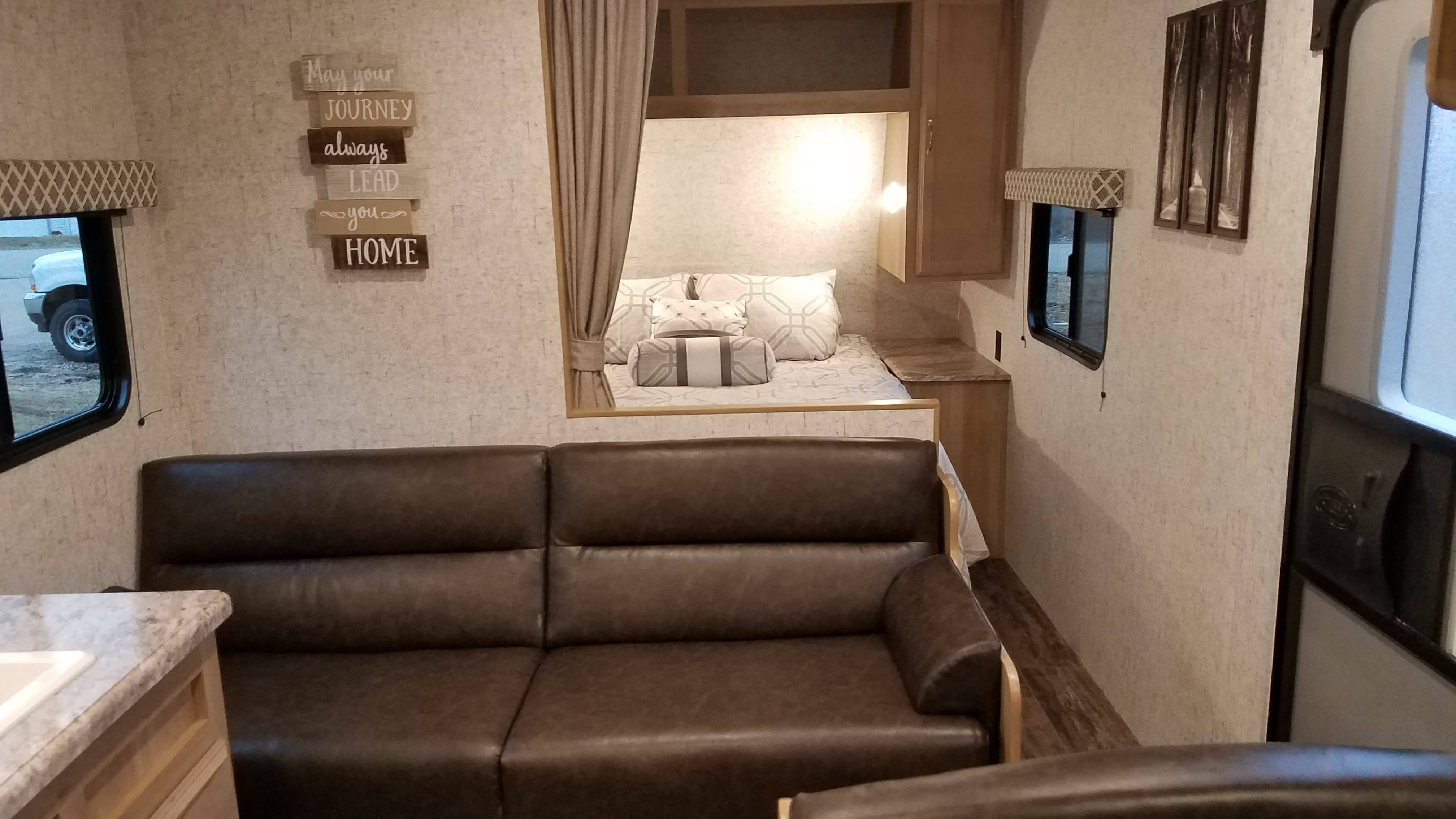 Cozy RV rental interior showcasing a spacious living area with a dark sofa, comfortable bed nook, and homey decor.. Braxton Creek 26BH 2019