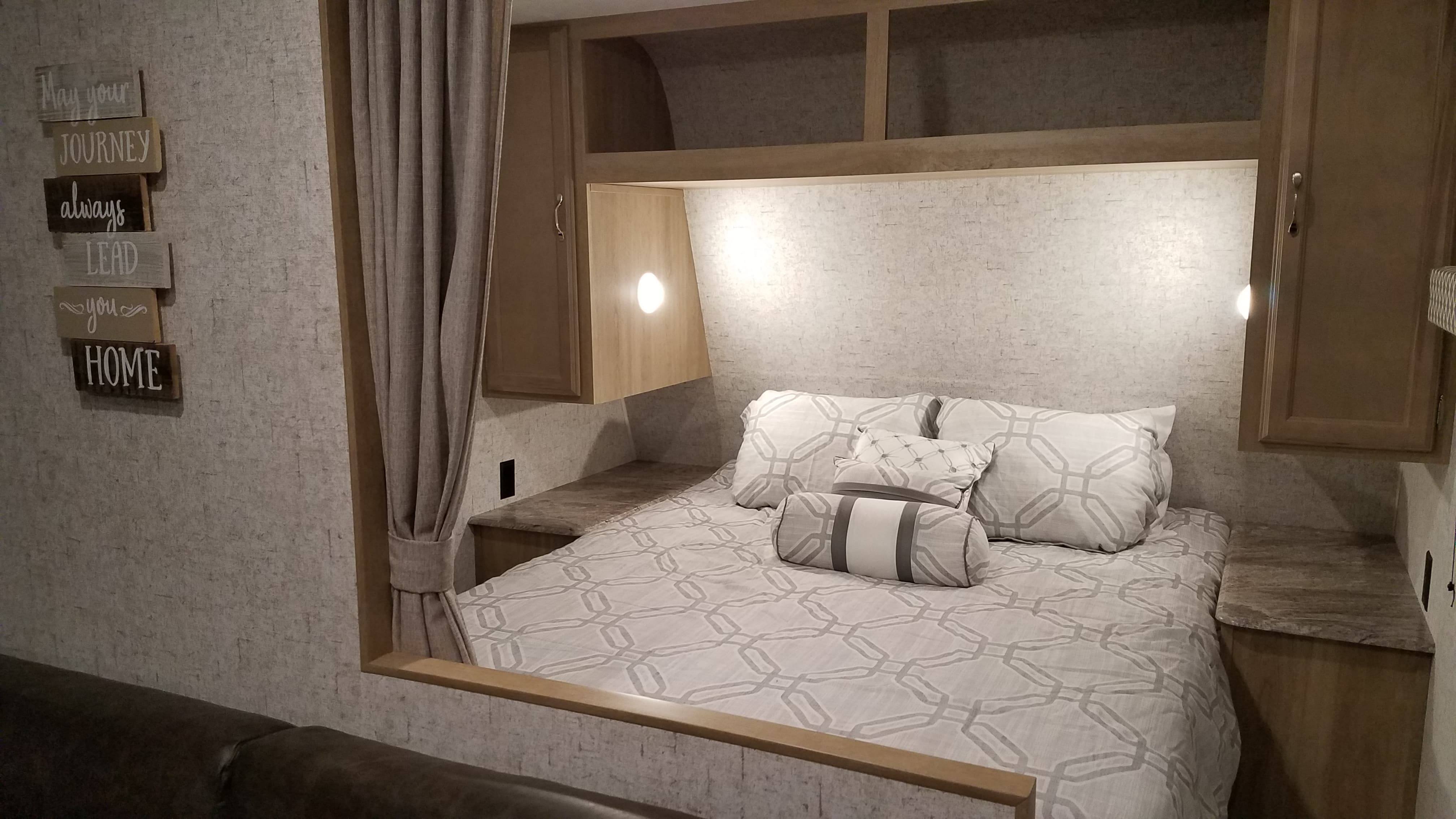 Inside a cozy RV rental: a bed with patterned bedding, built-in cabinets, sconce lighting, and a decorative wall hanging.. Braxton Creek 26BH 2019