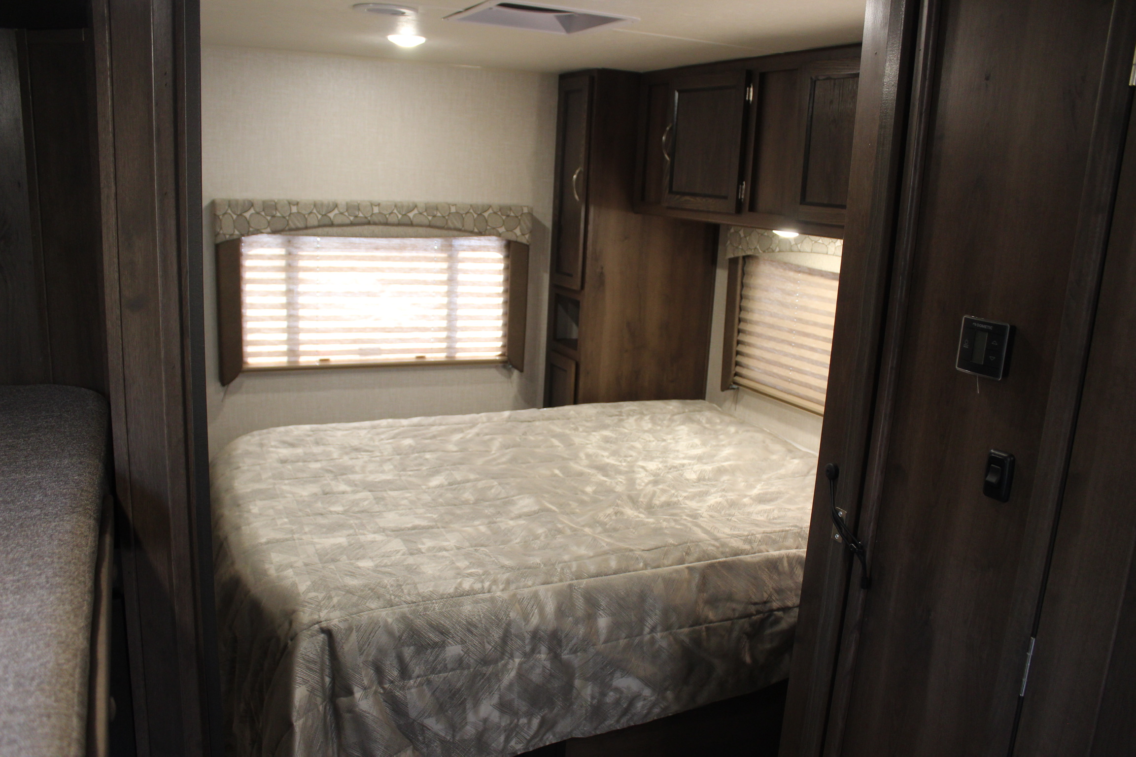 RV rental interior: cozy bedroom with a neatly made bed, window blinds, dark wood storage cabinets, and a side bunk.. Coachmen Freelander 2019