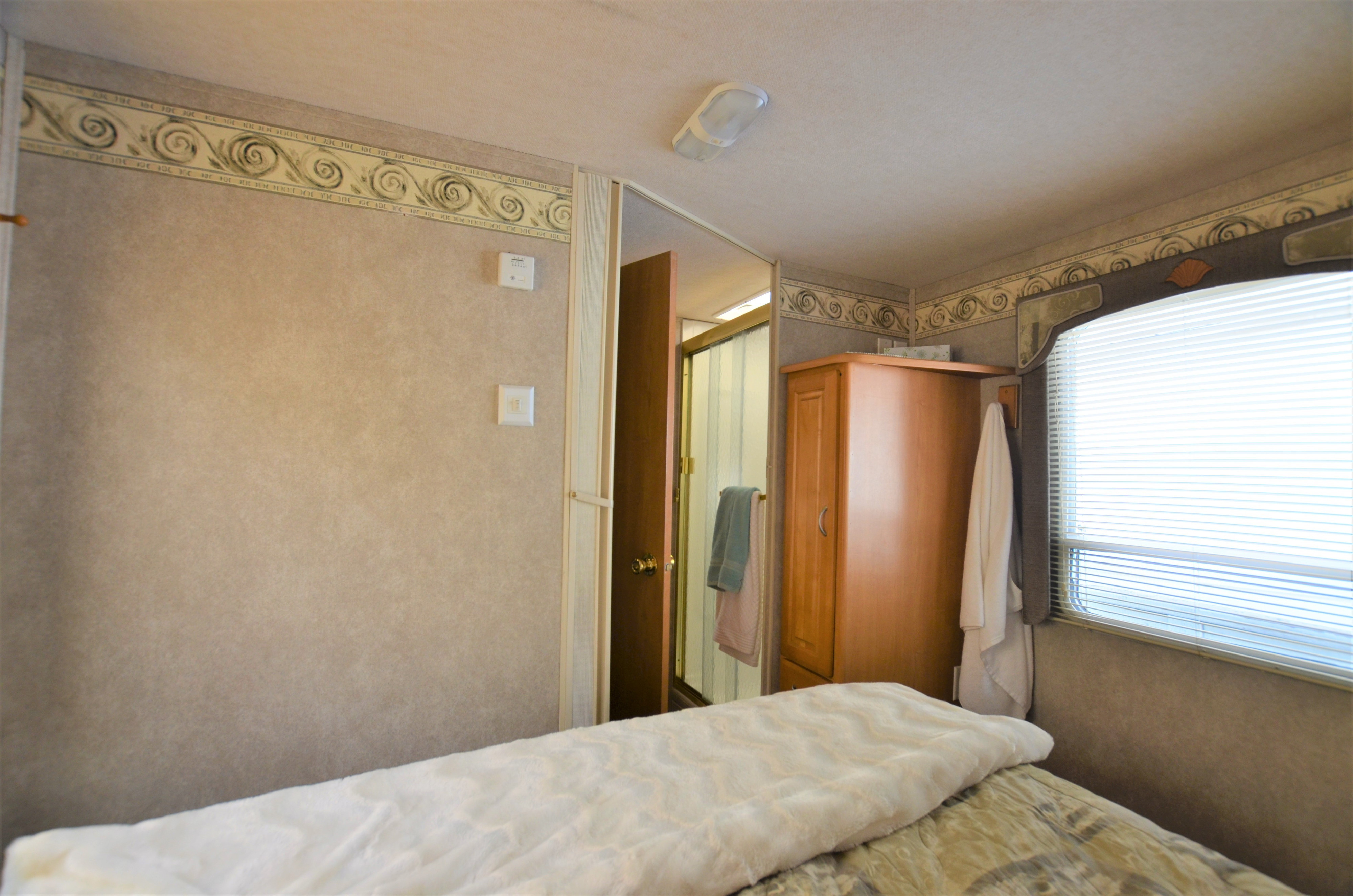 Cozy RV rental bedroom with a comfortable bed, window, small cabinet, and direct access to the bathroom.. Jayco Greyhawk 2005