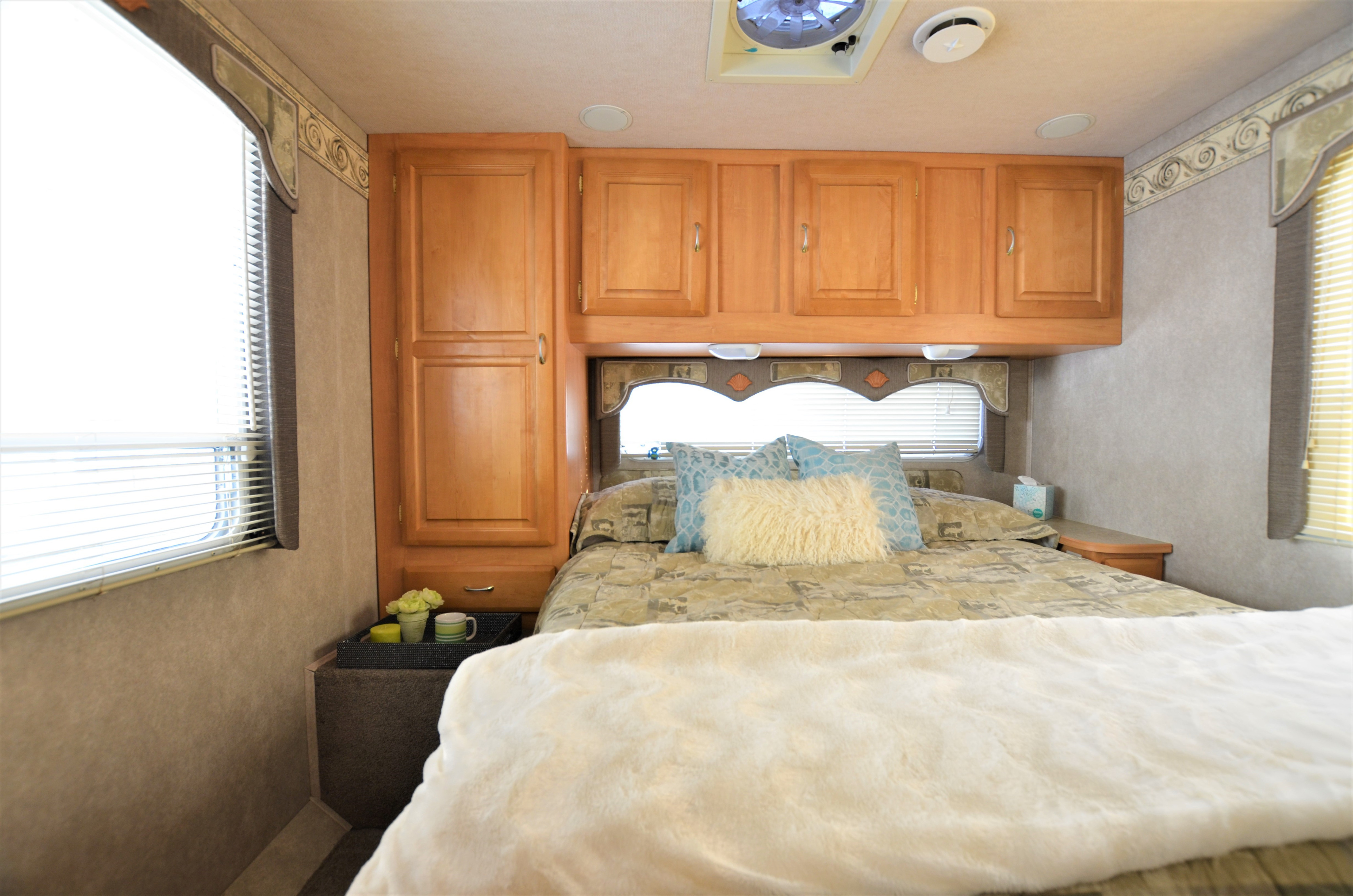 Cozy RV rental bedroom featuring a comfortable bed, ample cabinet storage, and bright natural light from the window.. Jayco Greyhawk 2005