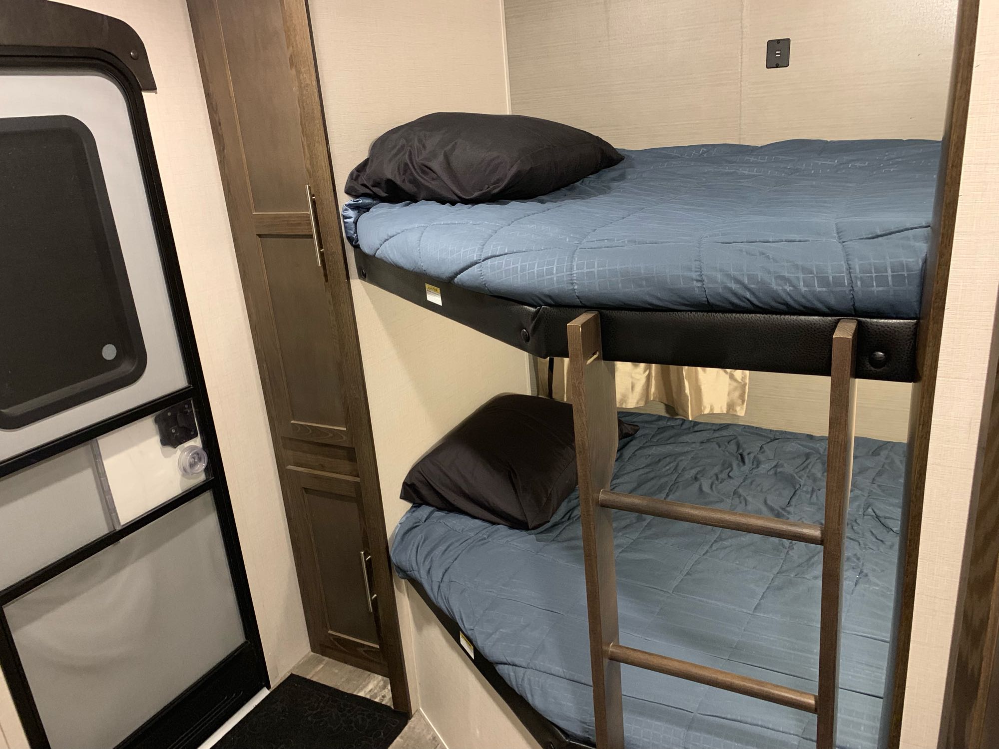 Cozy RV rental interior featuring bunk beds with blue bedding, a side cabinet, and the entry door, perfect for family sleeping.. keystone / Crossroads Volante 2019