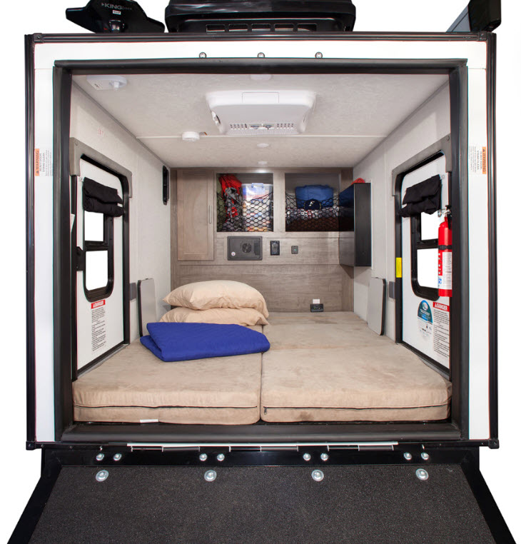 Compact RV rental interior with a bed, wall storage, dual side doors, and AC, viewed from the rear ramp.. Forest River No Boundaries 2019