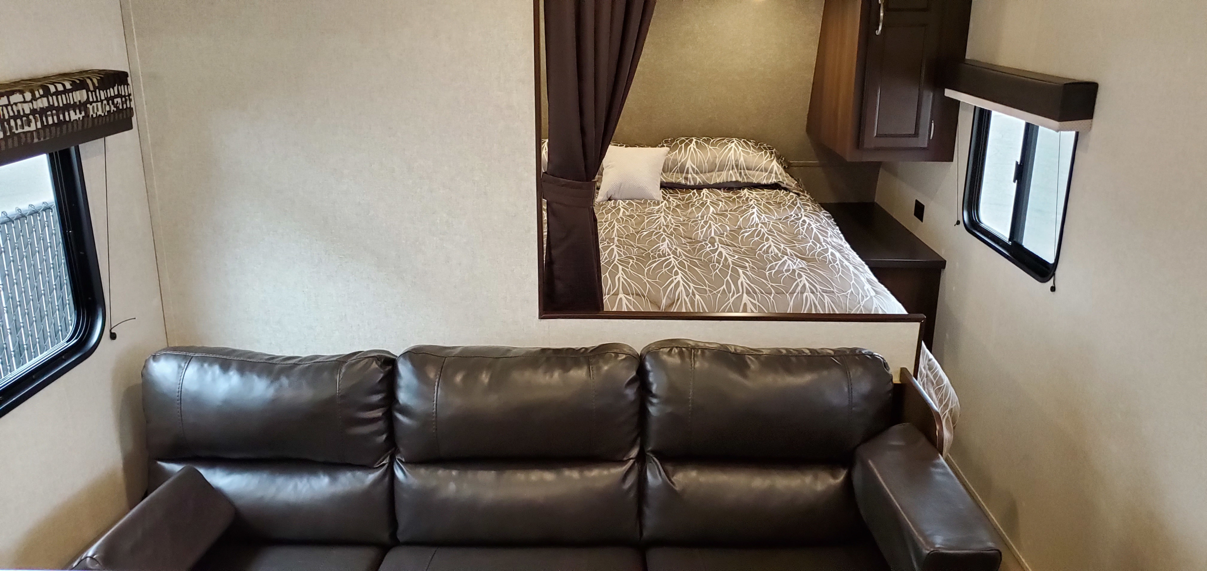 This RV rental interior features a cozy living area with a dark couch leading to a compact bedroom.. Jayco Jay Flight 2019