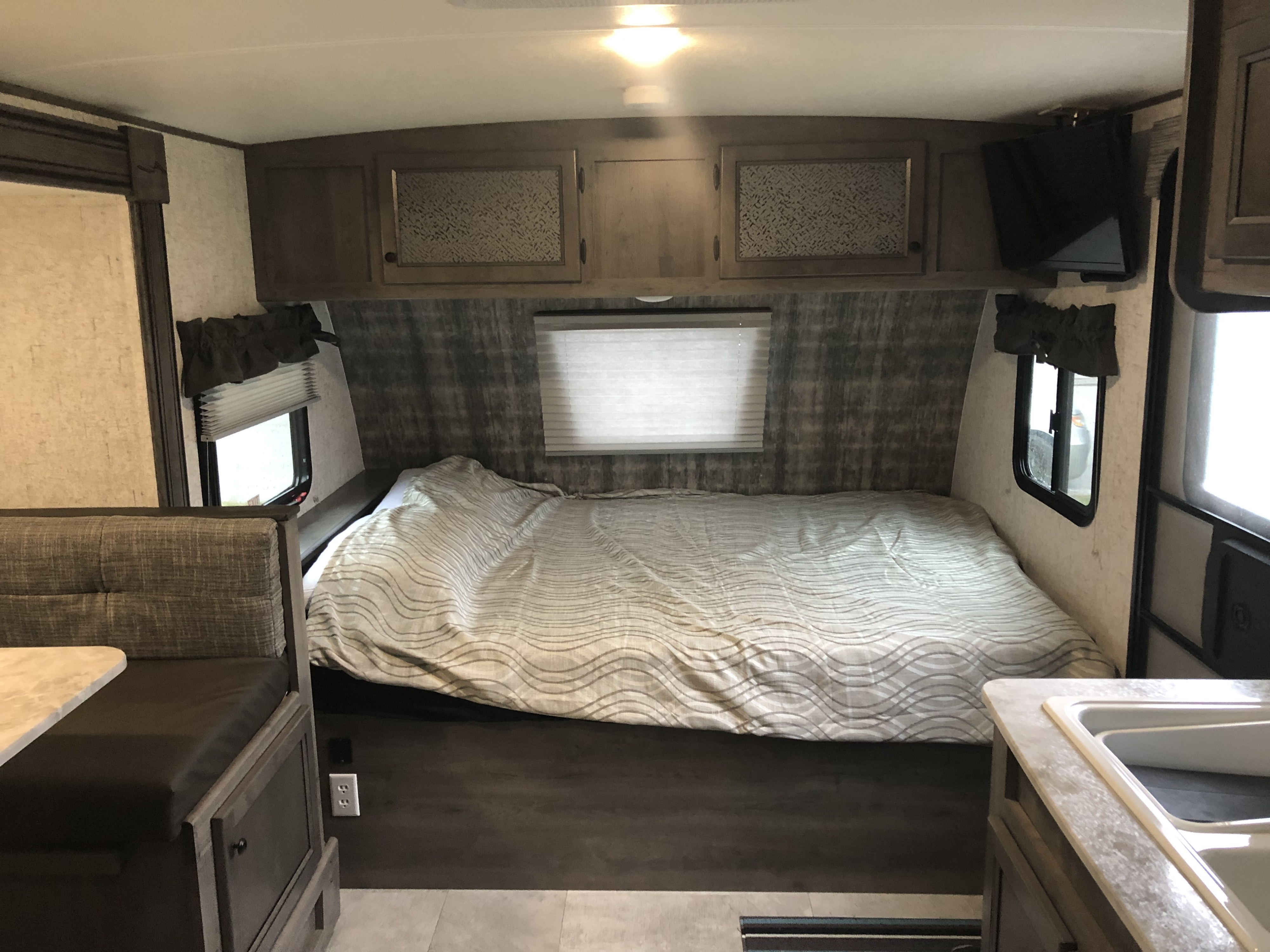 Cozy RV rental interior showing a comfortable bed, overhead cabinets, dinette area, and a compact kitchen.. Coachmen Apex 2020