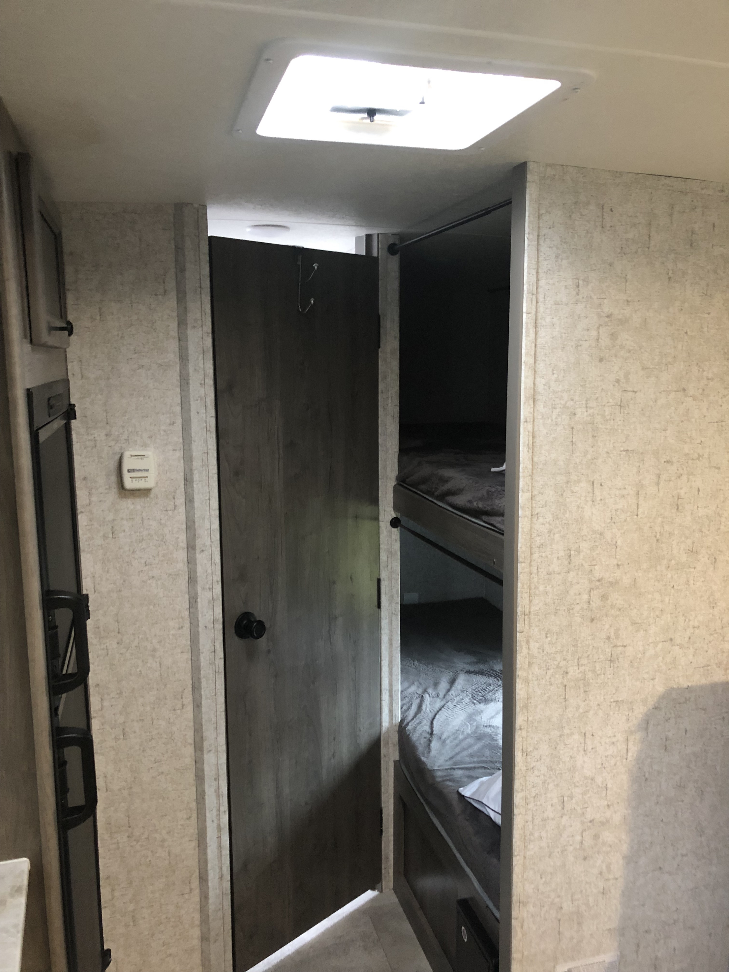 Interior of an RV rental featuring a set of bunk beds, a partially open door, and a thermostat on the wall, showcasing a compact and functional living space.. Coachmen Apex 2020