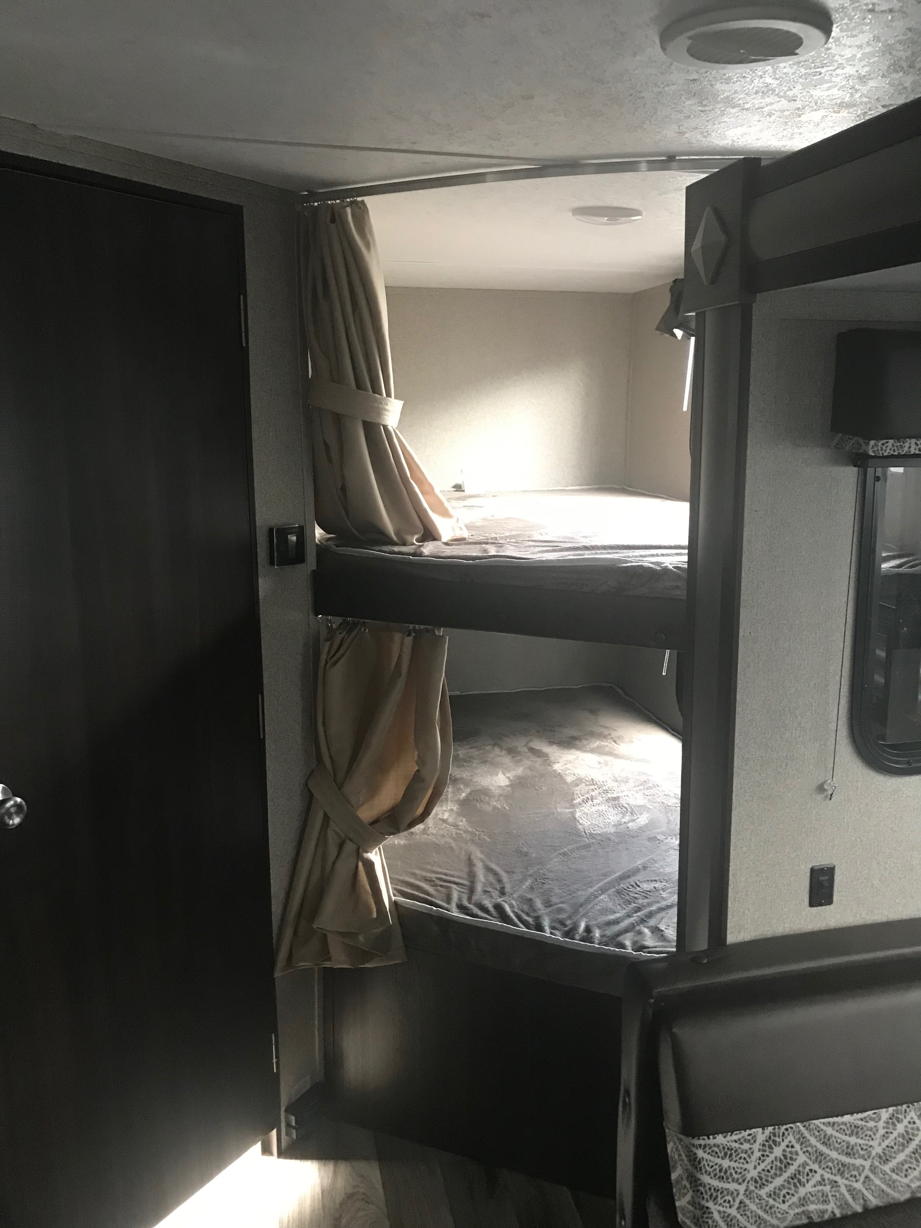 RV rental interior: two stacked bunk beds with curtains, ready for guests. Compact and practical living space with a door on the left.. Keystone RV Springdale 2019