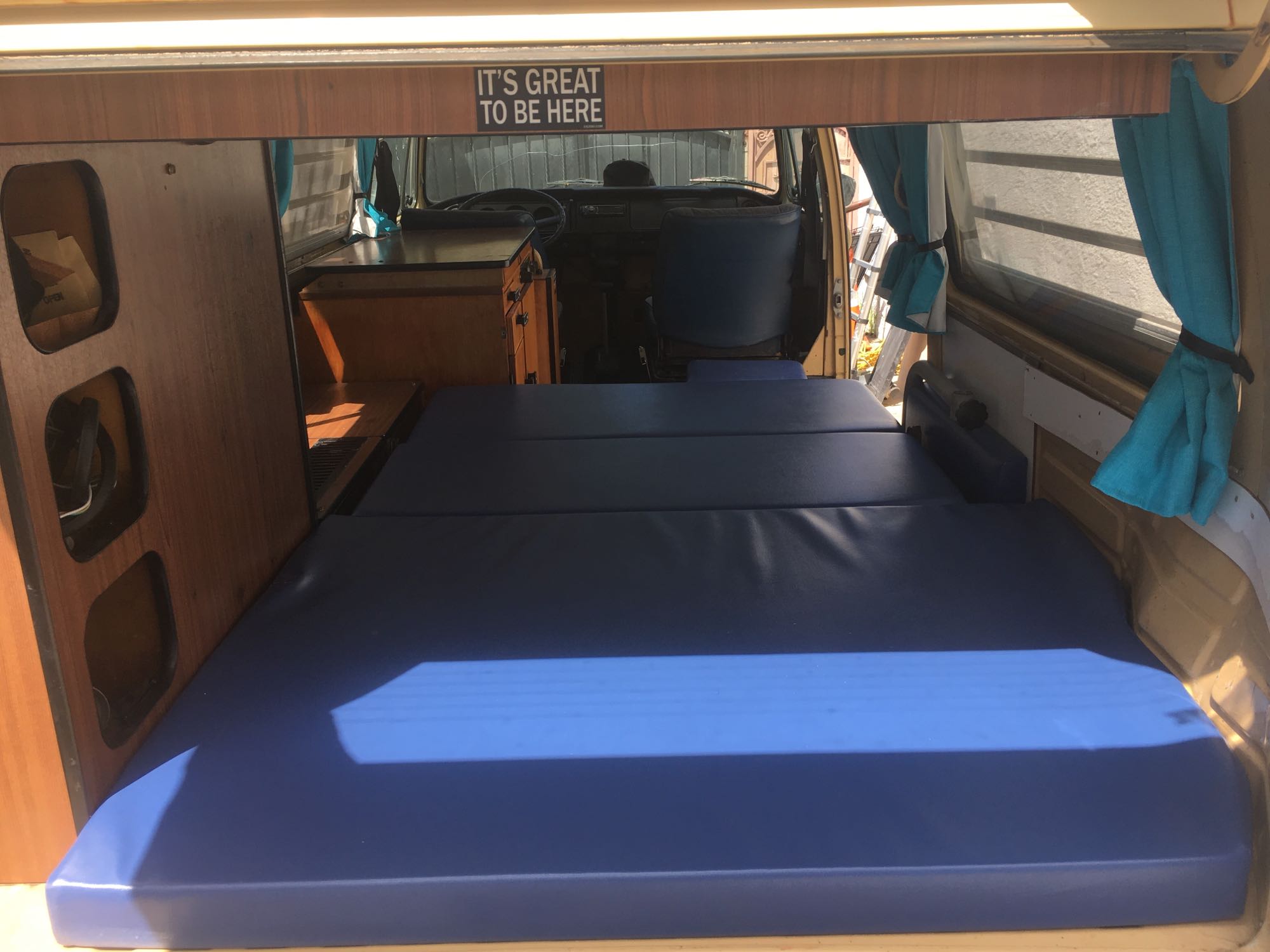 Inside a compact RV rental: a blue bed, wood storage, and view into the driver's cabin. Ideal for road trips.. Volkswagen Bus Westfalia 1979