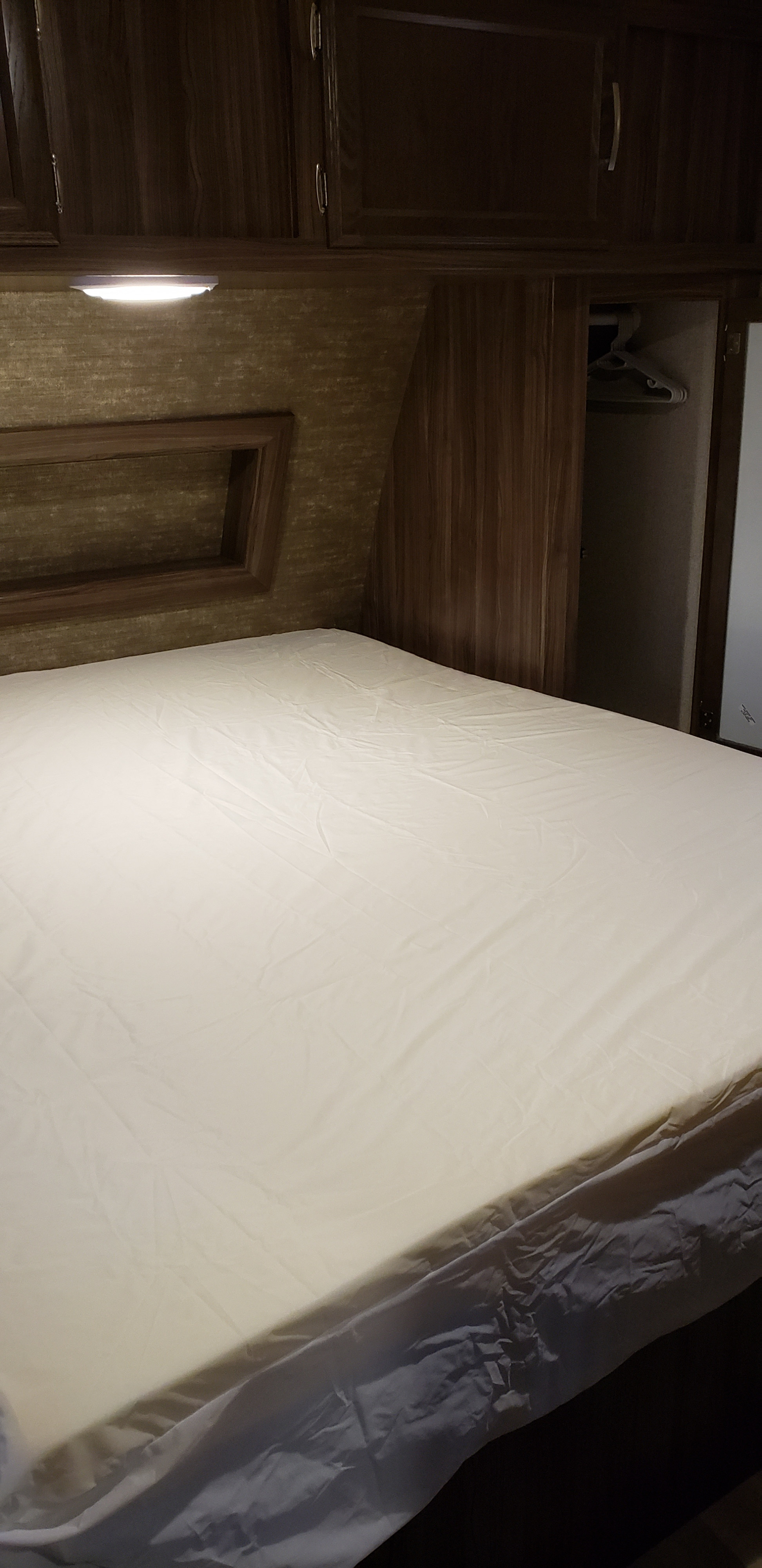 Cozy RV rental bedroom with a white sheeted bed, overhead wooden cabinets, reading light, and a closet.. Coachmen Apex 265rbss 2019