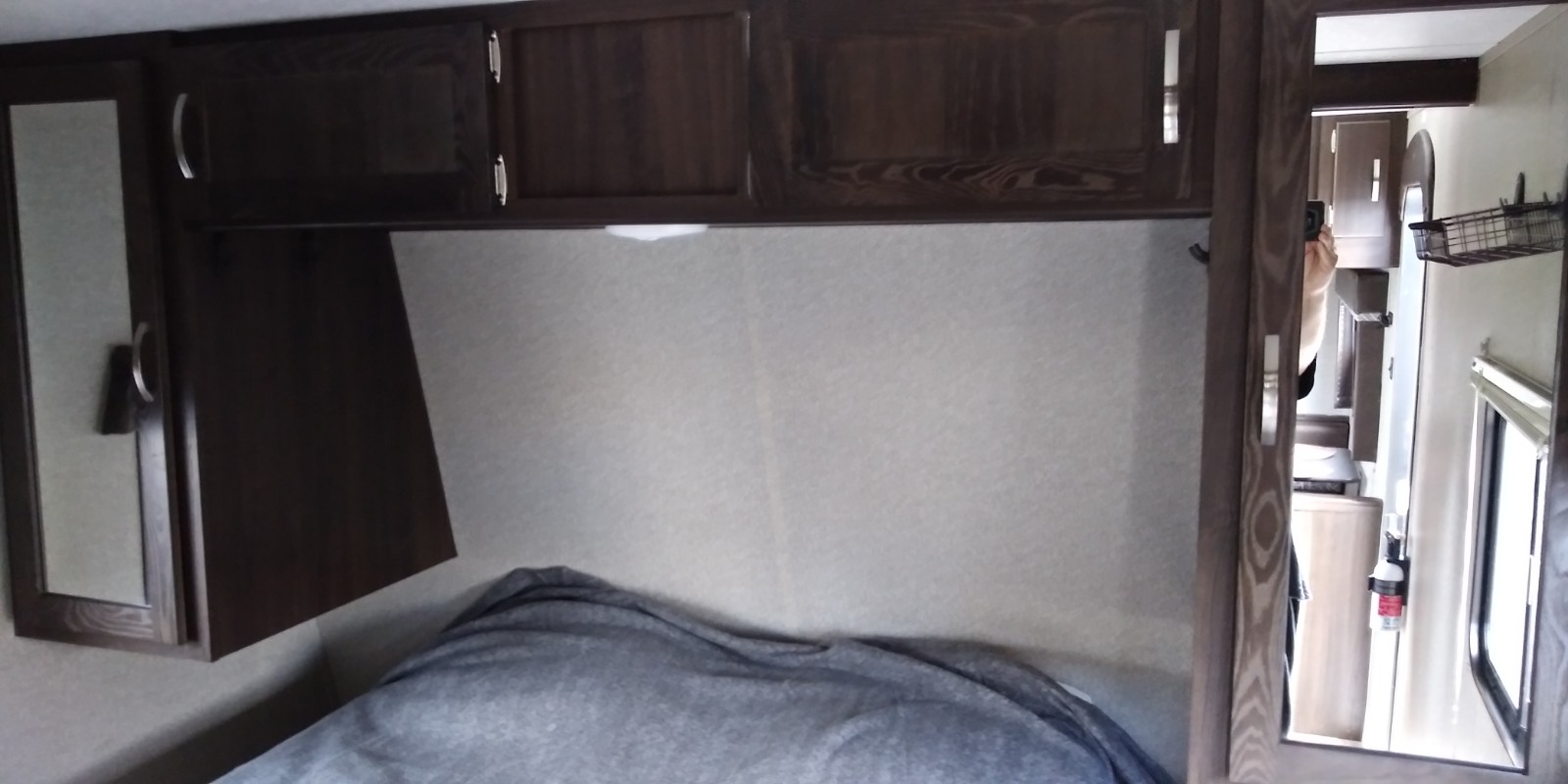 Compact RV rental bedroom with dark wood overhead cabinets and a cozy bed. A mirror shows more of the interior.. Keystone RV Springdale 2018