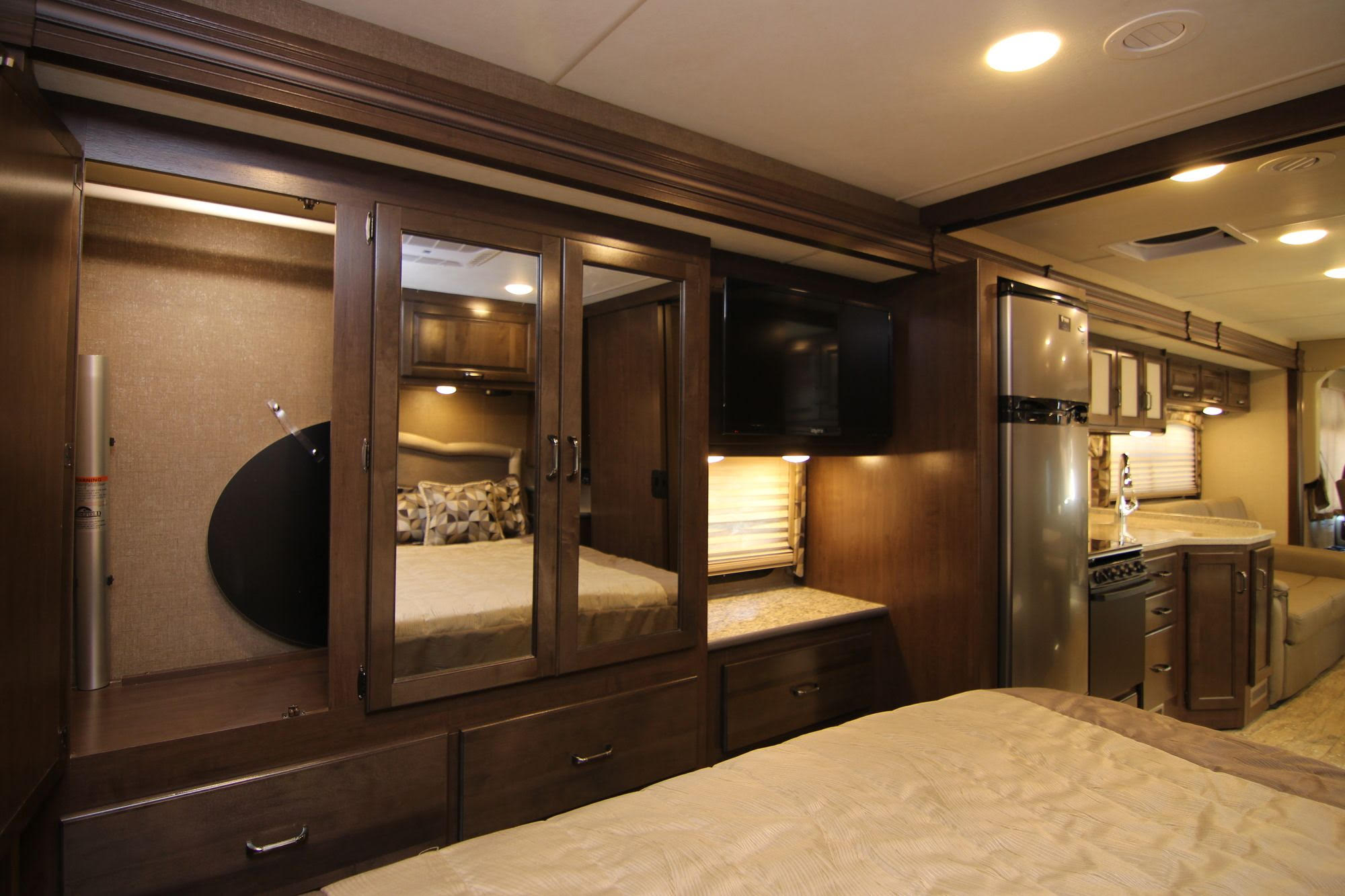 Spacious, modern RV rental interior showing a cozy bedroom, mirrored storage, entertainment center, and a glimpse of the kitchen.. Thor Hurricane 2018