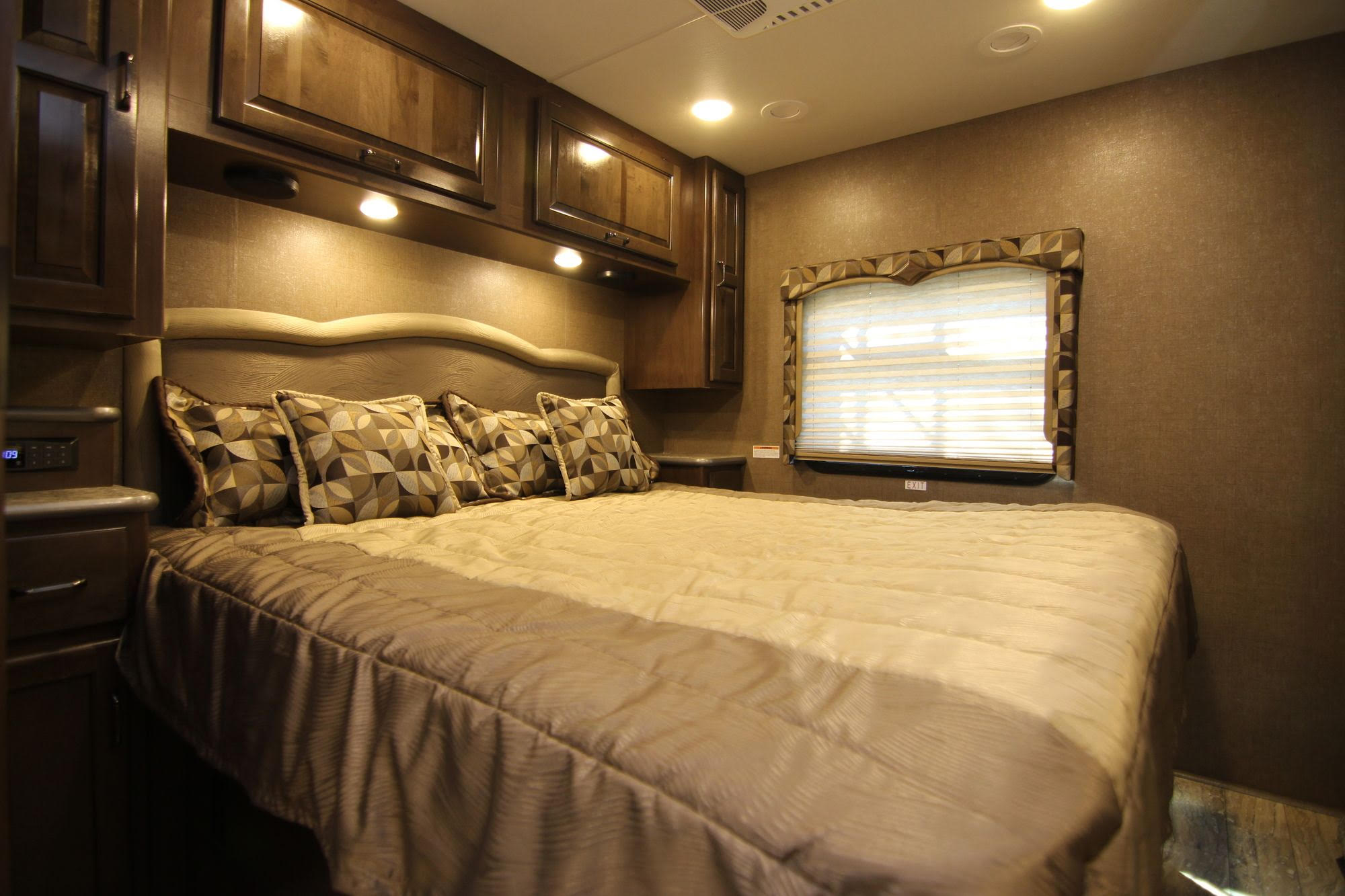 Comfortable RV rental bedroom with patterned pillows, wooden cabinets, window blinds, and overhead lighting for travel.. Thor Hurricane 2018