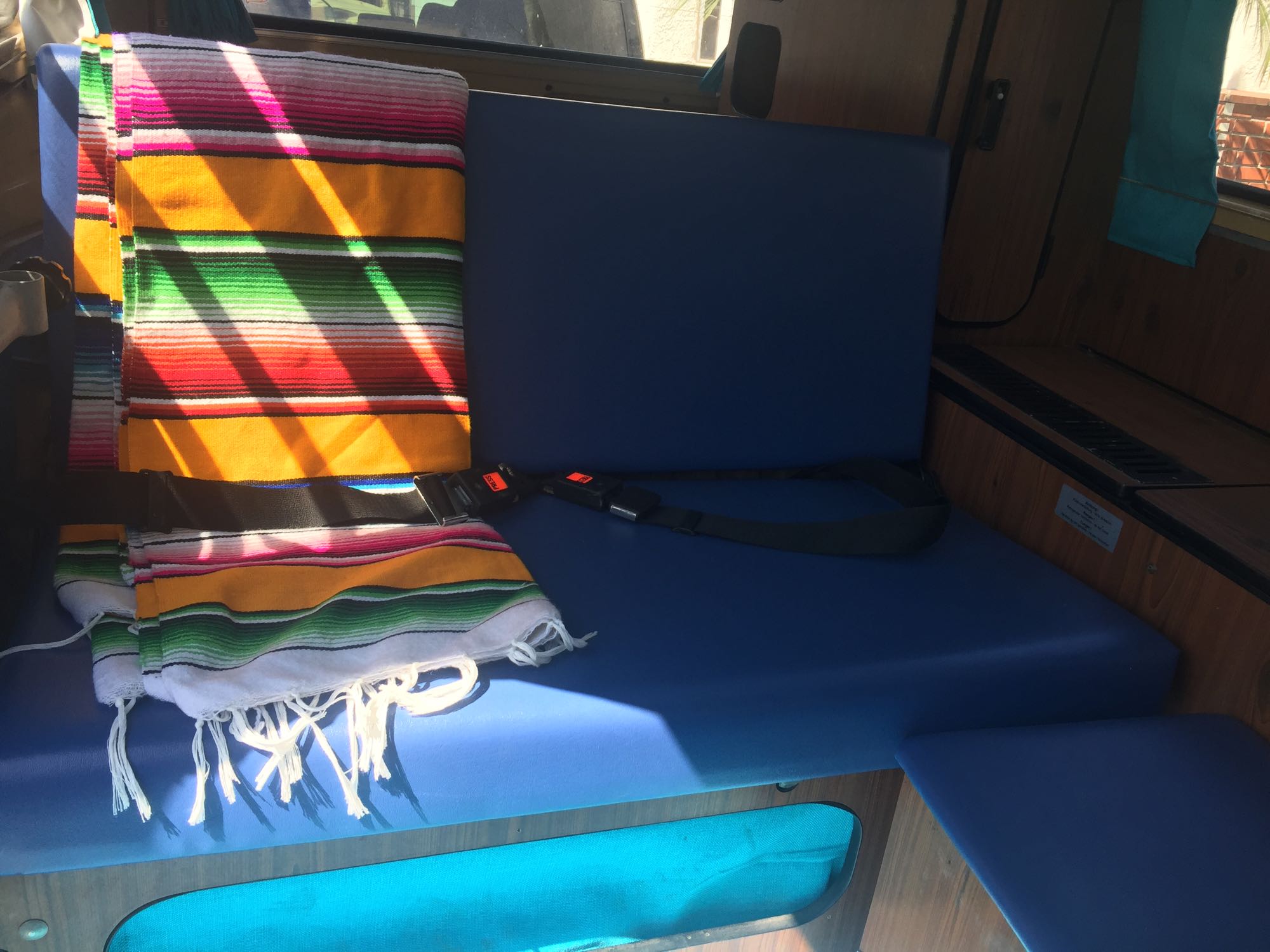 RV rental interior with blue seats, a colorful serape blanket, and safety seatbelts.. Volkswagen Bus Westfalia 1979