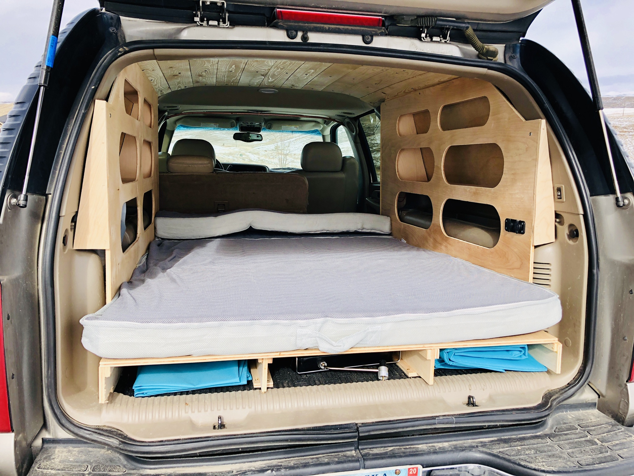 Interior of an SUV converted into a custom camper bed with storage, an ideal RV rental alternative for road trips.. Chevrolet Suburban Overland 2001